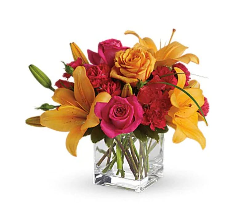 Uniquely Chic - Uniquely beautiful and uniquely bright, this is a bona fide bombshell of a bouquet. Brilliant blossoms are perfectly arranged in an exclusive cube vase. Orange roses, hot pink roses and spray roses are joined by glowing orange asiatic lilies and bear grass in a delightful vase. This unique arrangement is delivered in a cube but it's definitely not for squares.   Orientation : All-Around  All prices in USD ($)