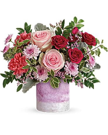 Washed In Pink Bouquet - When you want to make them feel extra special, think pink! This pretty present of pink roses and lavender blooms is arranged in a hand-blown, art-glass vase with frosted finish and the prettiest shade of pink. Pink roses, dark pink spray roses, pink carnations, lavender cushion spray chrysanthemums and lavender limonium are arranged with dusty miller, huckleberry and pitta negra. Delivered in an Orchid Color Frost Art Glass cylinder. 