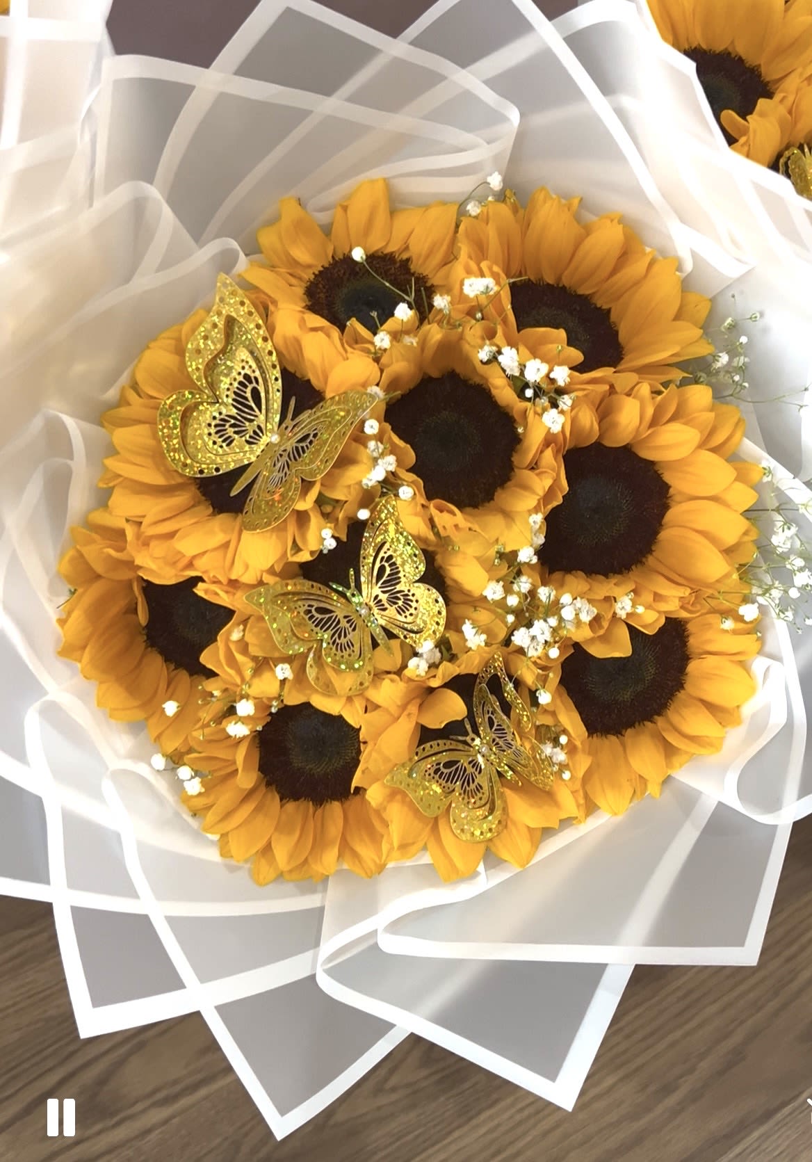 Golden Whisper - Radiant and full of joy, this stunning bouquet features 10 vibrant sunflowers symbolizing warmth and positivity, delicately surrounded by soft white baby’s breath for a touch of lightness and charm. Three shimmering golden butterflies dance gracefully among the blooms, adding an enchanting accent that captures the beauty of sunshine and transformation. Perfect for brightening any space, celebrating a special occasion, or simply sharing happiness with someone who makes life shine a little brighter.