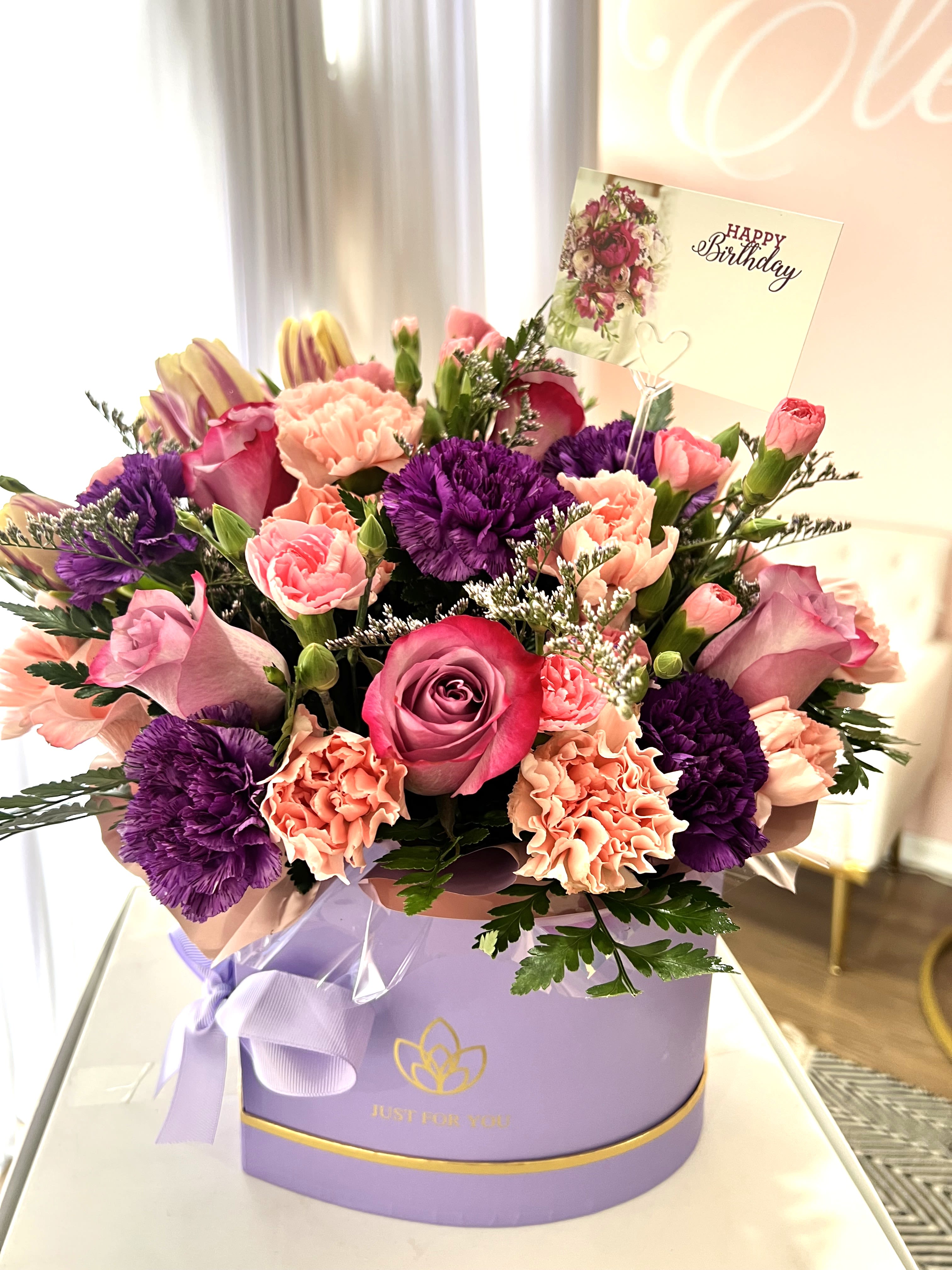 Elegant Blossom Box - This stunning arrangement showcases a lovely variety of fresh flowers in delicate shades of purple and pink. Designed in an elegant box, it combines roses, carnations, and seasonal blooms to create a soft and sophisticated look. A perfect gift to celebrate the beauty, strength, and love of the special women in your life. 