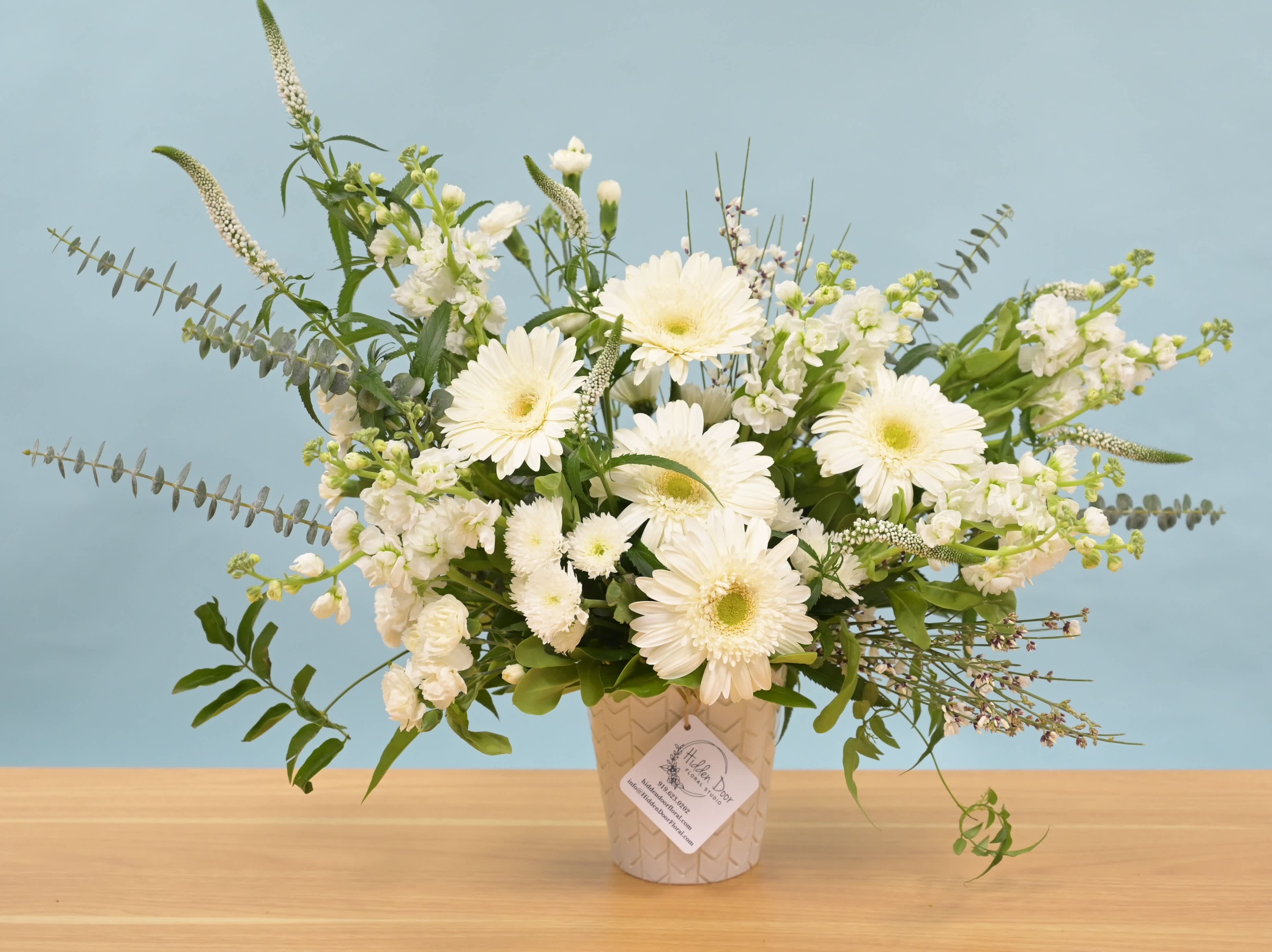 Ivory Serenade - Ivory Serenade White and green is one of the most quietly confident color combinations in floral design. No drama, no competition — just the kind of arrangement that makes a room feel like someone thought carefully about it. Ivory Serenade is airy and textural, with sculptural layers that catch light differently depending on where you're standing. Soft, unhurried, and genuinely graceful — the kind of piece that works for thoughtful gifting, sympathy, or a home that simply deserves something serene. Available for same-day flower delivery in Raleigh, Cary, Durham, Chapel Hill, Morrisville, Apex, and Wake Forest when ordered before 2 PM. Please Note: Handcrafted for every order. Flower varieties and textures follow what's most beautiful that day — the ivory and green palette holds throughout. Vessels may vary.