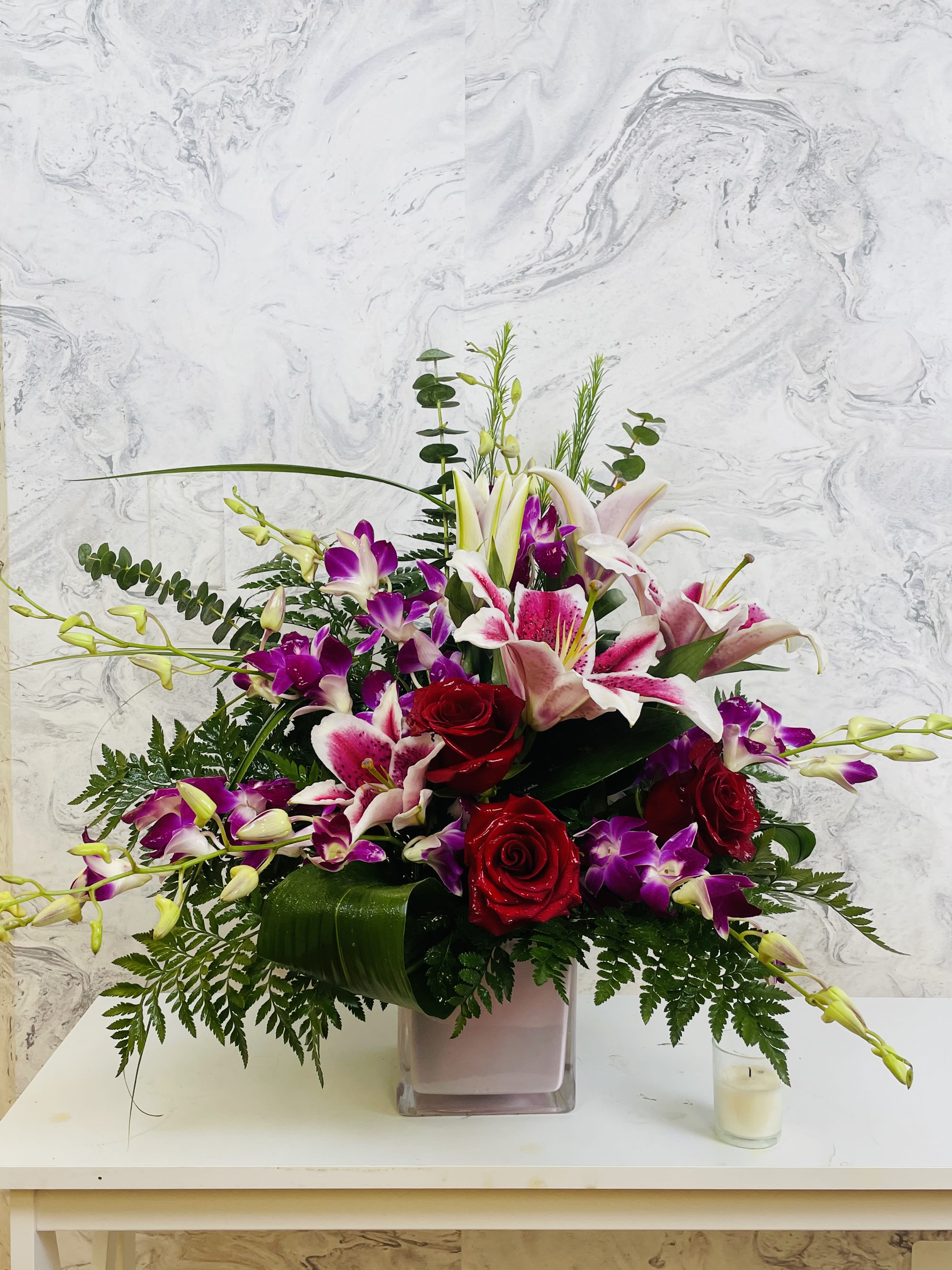 Blooming Symphony  - Welcome to Blooming Symphony, your gateway to the enchanting world of floral elegance. Immerse yourself in the breathtaking beauty of stargazer lilies, purple orchids, and red roses. Our carefully curated collection of exquisite blossoms will transport you to a realm of captivating fragrances and vibrant colors. Whether you seek the perfect arrangement for a special occasion or simply desire to indulge in nature's marvels, Blooming Symphony is your destination for floral bliss. Discover the harmonious blend of grace, sophistication, and passion that these extraordinary flowers embody, and let them grace your life with their timeless allure. The container may change but the same quality and value 