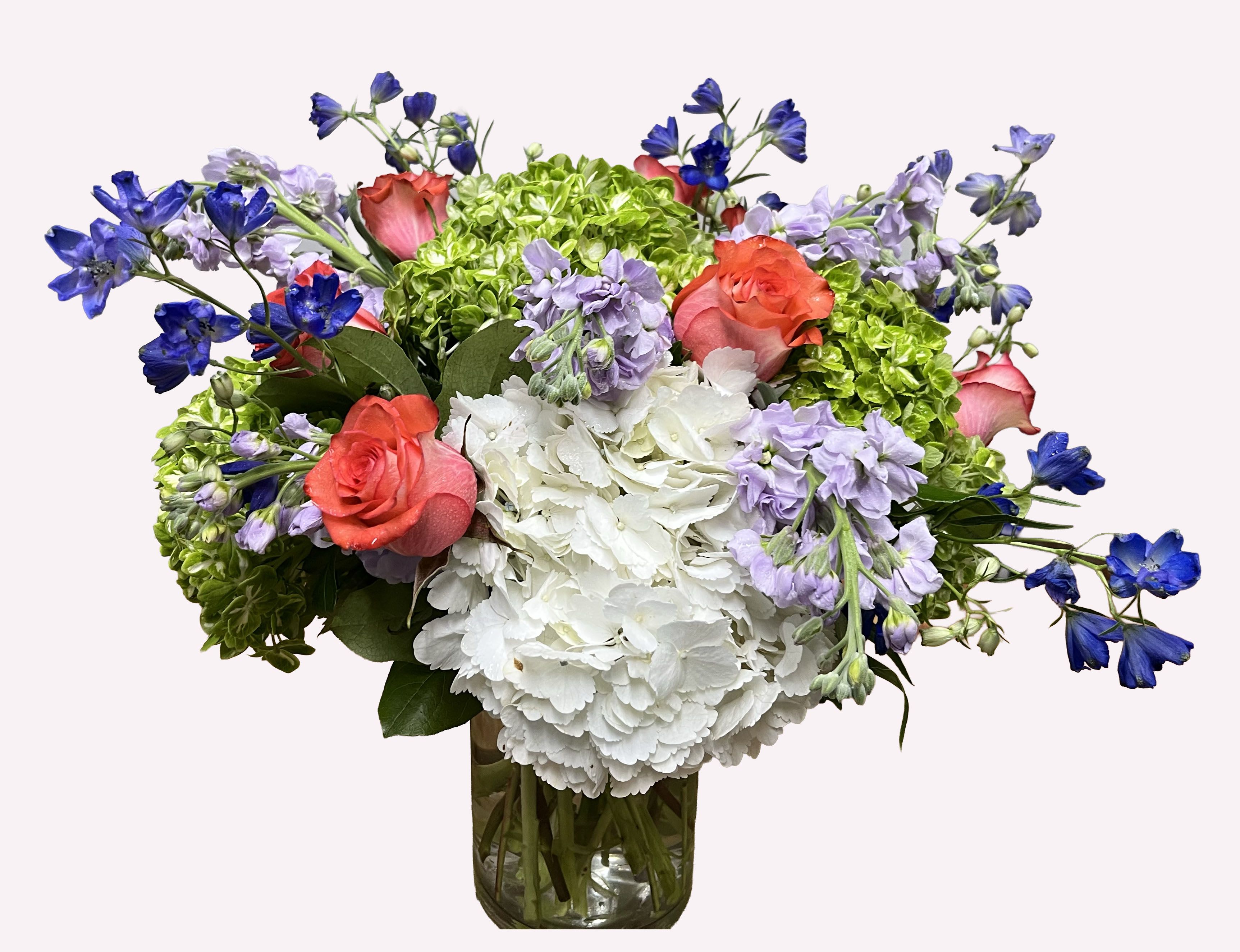Whimsical Garden - Exclusively at James Weir, this new creation inspires a feeling of spring gardens with its whimsical look! A combination of soft lavender stocks and white hydrangeas, along with vibrant blue wild delphiniums, peach-orange roses, and shamrock green hydrangeas, arranged in a glass vase.