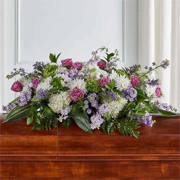 Lavender, pink, and white casket spray with roses, mums, hydrangeas and asters on a wooden casket