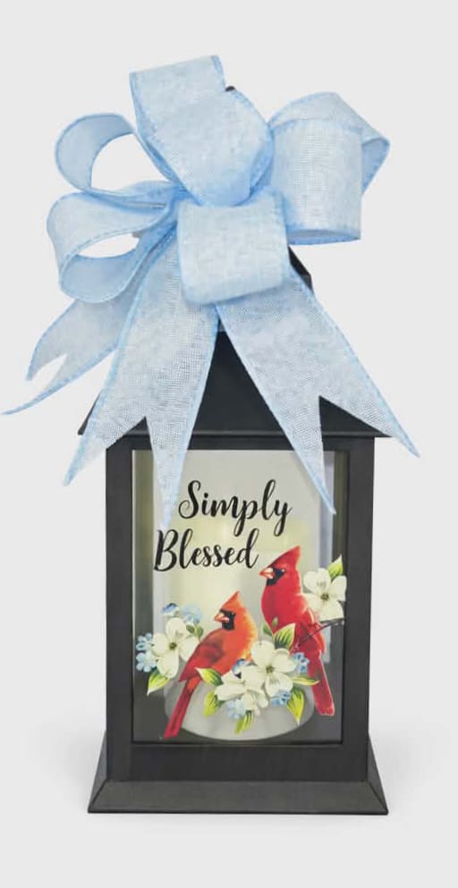 Simply Blessed Lighted Lantern - Message on Lantern reads " Simply Blessed". These lanterns are made of weather friendly materials and UV printed glass. They include a flameless LED candle with a built-in automatic timer: 6hrs ON/18hrs OFF (3 AAA batteries are included). They are suitable for hanging or free-standing use. Comes with a bow, if you would like a specific color bow let us know in note section. H: 9" DIA: 4 "
