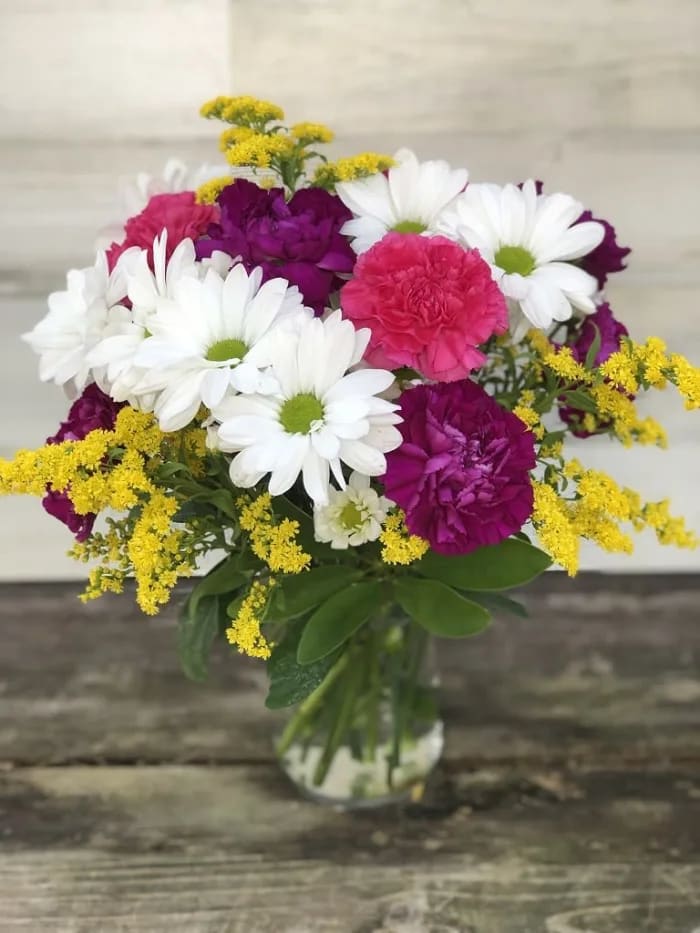 Bouquet of white daisies, pink carnations, and yellow filler in a glass vase