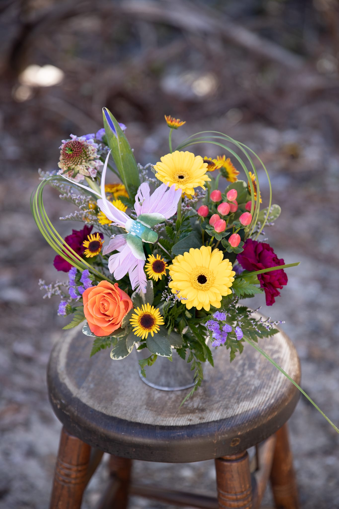 Mixed bouquet with yellow daisies, orange rose, and purple accents in a metal container