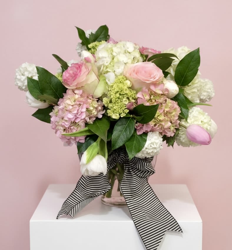Pink and white roses, hydrangeas, and tulips in a glass vase with a striped ribbon
