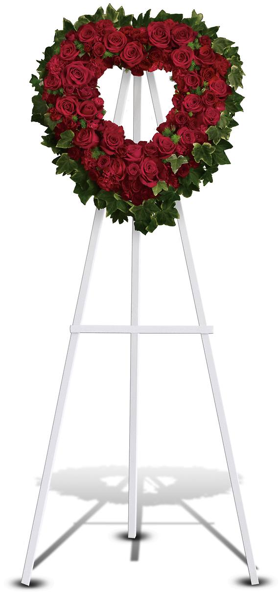 BLESSED HEART - Make a strong, stylish statement of love with this beautiful heart-shaped wreath. Presented on a funeral easel, the rich red rose sympathy arrangement is a lovely standing spray to place on the altar or by the entrance to the service.  Red roses and carnations are accented with ming fern and variegated ivy on an open heart-shaped wreath.