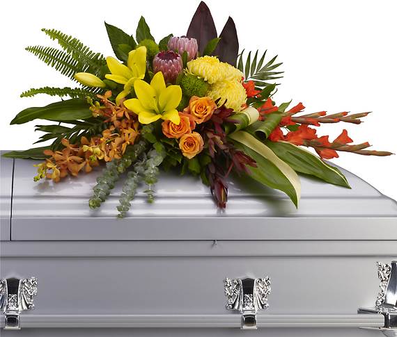ISLAND MEMORIES CASKET SPRAY - Tropical flowers evoke tropical breezes in this modern style casket spray. Deep red ti leaves and aspidistra leaves frame fresh and fragrant yellow lilies and chrysanthemums, along with orange orchids, roses and red gladioli.  
