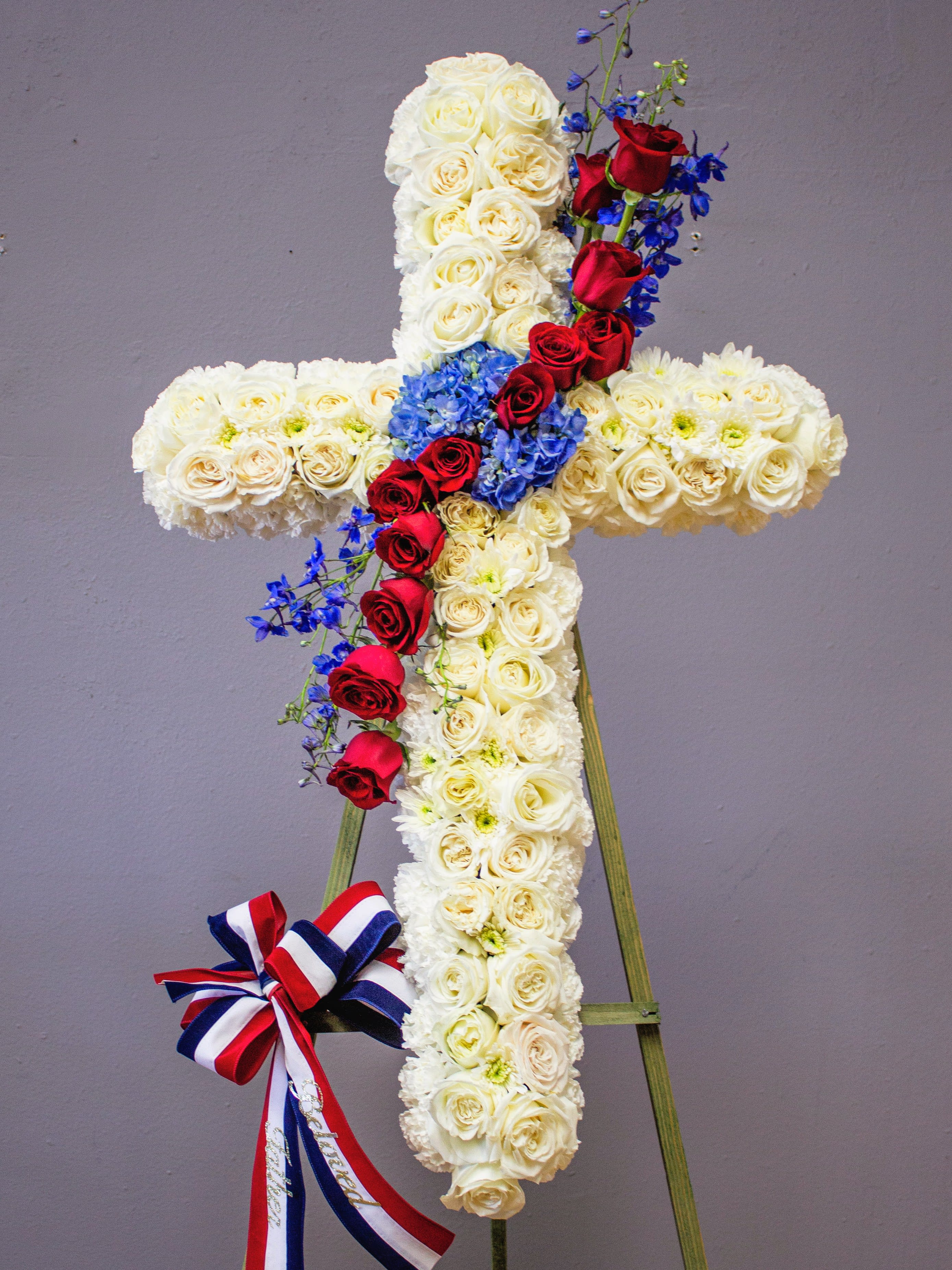 FUNERAL CROSS - Honorable Goodbyes 52 - This is a wonderful option for a funeral service, church or graveside. This standing cross will be designed with an 18", 24” or 30" cross form and will be delivered on a stand. This lovely mix of red, white and blue flowers of roses, mums and carnations is the perfect way to honor your loved one.   **This is a piece for a funeral or memorial service. Please place the order at least 2 days prior to the service to guarantee a certain arrangement. Anything sooner and we cannot guarantee it will match the picture. These pieces can be customized to the color of your choice. The flowers may vary depending on availability of the flowers, special requests and quality of the flowers we have in stock. If you have a special request please add it to our special instructions when placing your order. If you have any questions please don’t hesitate to call. 714 289 1123**