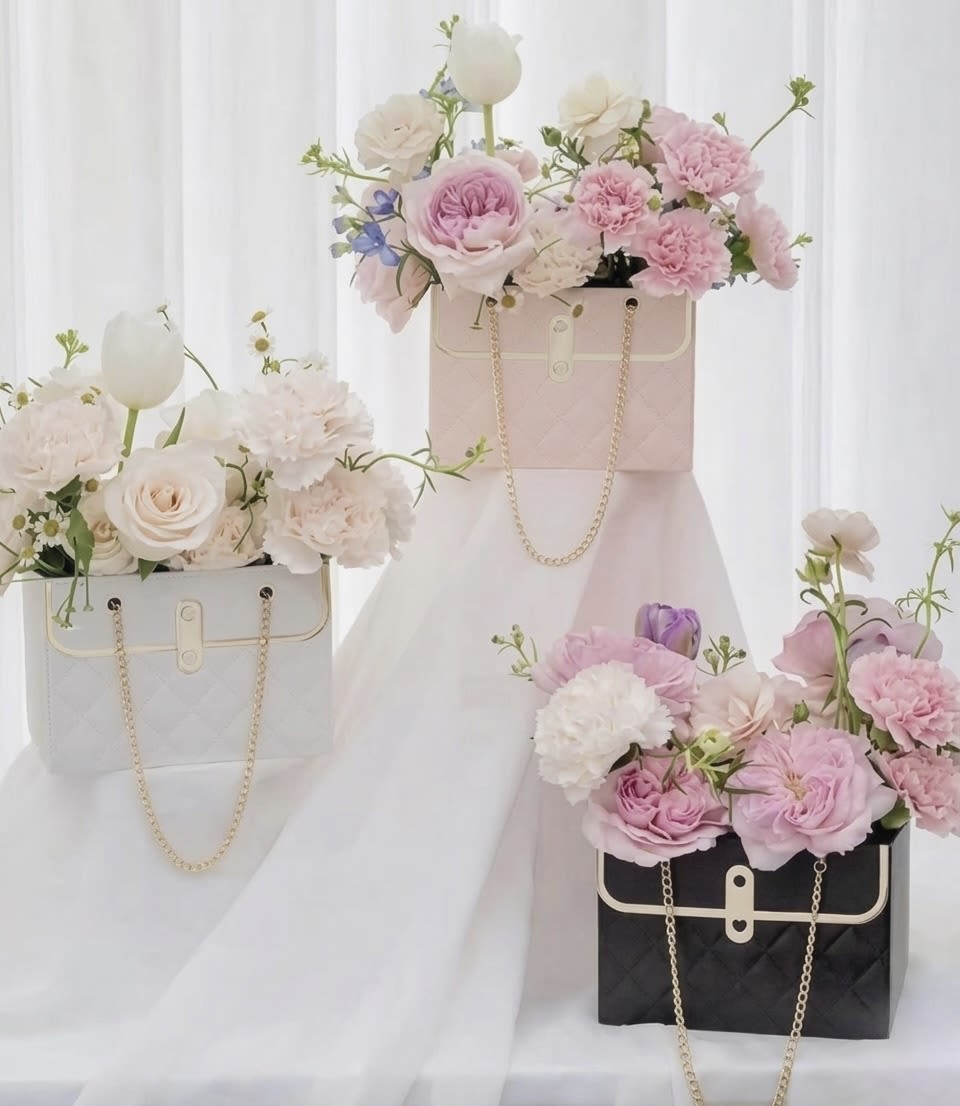 Luxury Handbag Rose Box – Designer Floral Gift - Elevate your gift with our Luxury Handbag Rose Box, a designer-inspired floral arrangement crafted for those who appreciate elegance and sophistication.  This modern handbag-style box features premium fresh roses beautifully arranged inside a quilted luxury base with gold hardware and chain detail. The structured design creates a high-end aesthetic that blends fashion and floral artistry into one unforgettable statement piece.  Available in pink, white, or black box options, allowing you to choose the style that best matches your occasion. Rose colors may vary based on availability to ensure freshness and premium quality.  Perfect for birthdays, anniversaries, Valentine’s Day, Mother’s Day, luxury surprises, or any moment that deserves something extraordinary.  Handcrafted by AMORE in Nashville, Tennessee. Available for local flower delivery in Nashville and surrounding areas.
