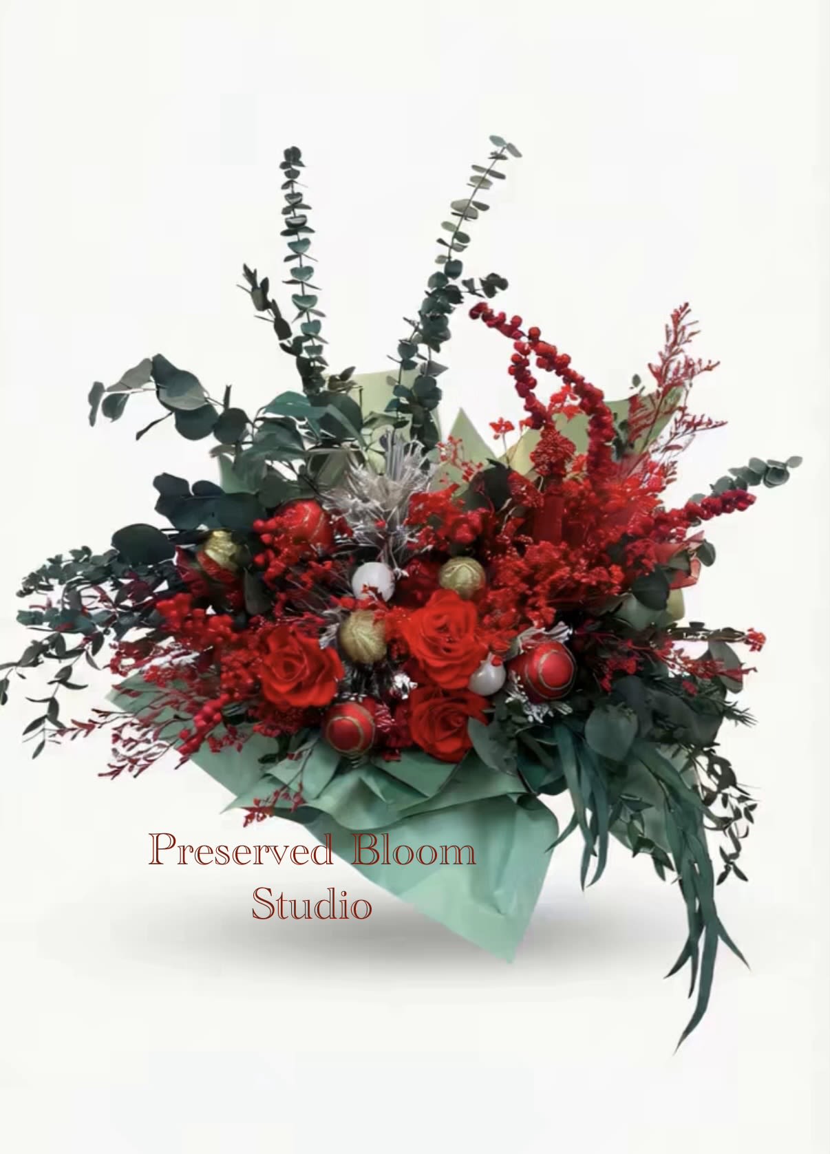 Christmas Arrangement  - This is a Christmas-themed basket, mainly composed of red roses, eucalyptus leaves, red berries and other flower materials. Red roses symbolize love and romance. Eucalyptus leaves (eucalyptus leaves) add a winter atmosphere and a sense of luxury to the bouquet with their unique aroma and elegant silver-green tone. Red berries (such as holly or similar artificial berries) are dotted, creating a strong festive atmosphere. The bouquet also contains silver decorations (such as balls or glittering twigs) and green wrapping paper, which further enhances the festive color of Christmas (red, green and white/silver are the traditional colors of Christmas). This style of bouquet is often used for church Christmas decorations, holiday gifts or company openings.
