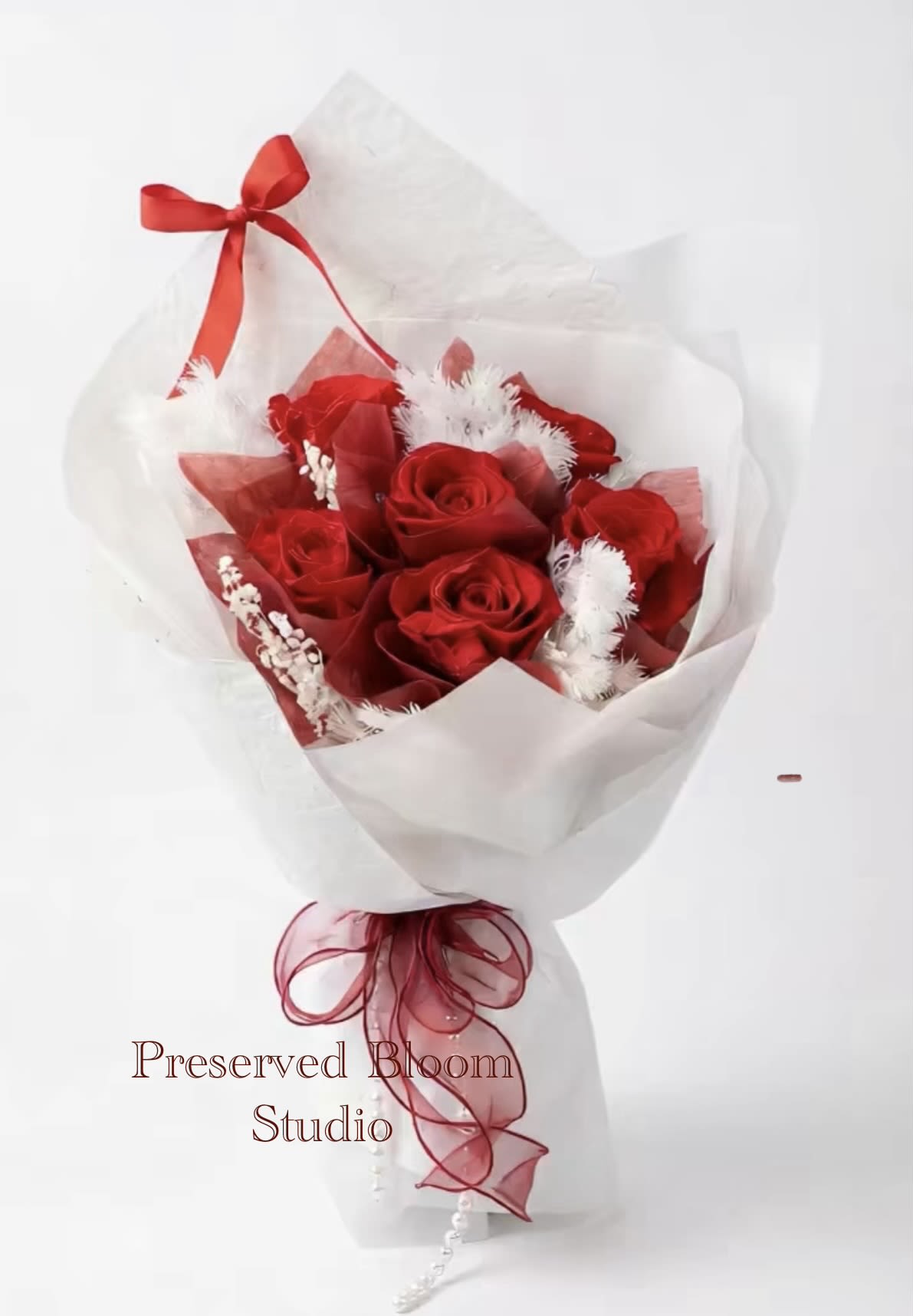 Red Whisper - This shows a bouquet of bright red roses wrapped in white wrapping paper, with red lining paper and white pontoise, and a red ribbon is tied at the bottom of the bouquet to form an elegant knot. It has a very romantic atmosphere.