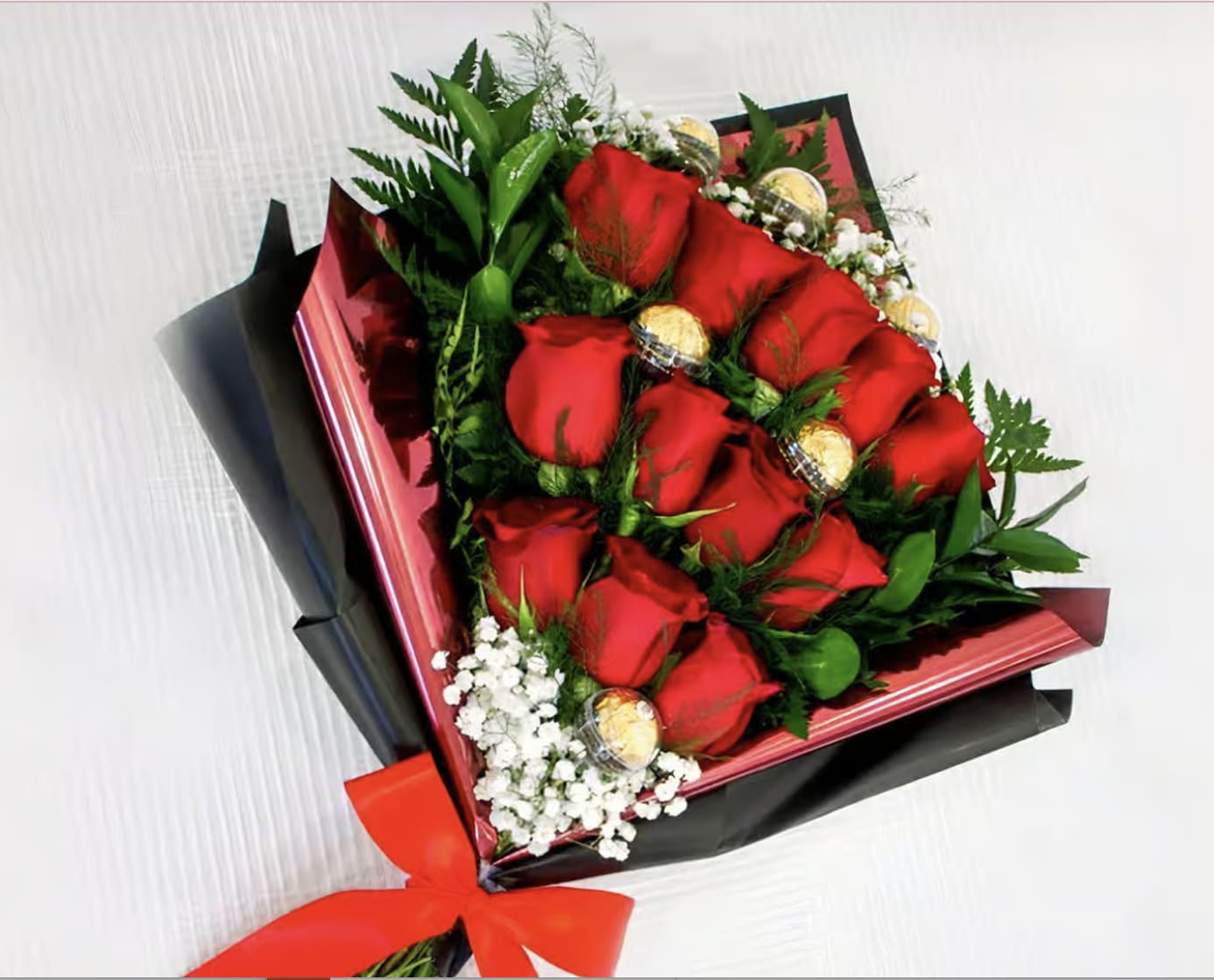 Bouquet of red roses with gold-wrapped chocolates and white filler flowers