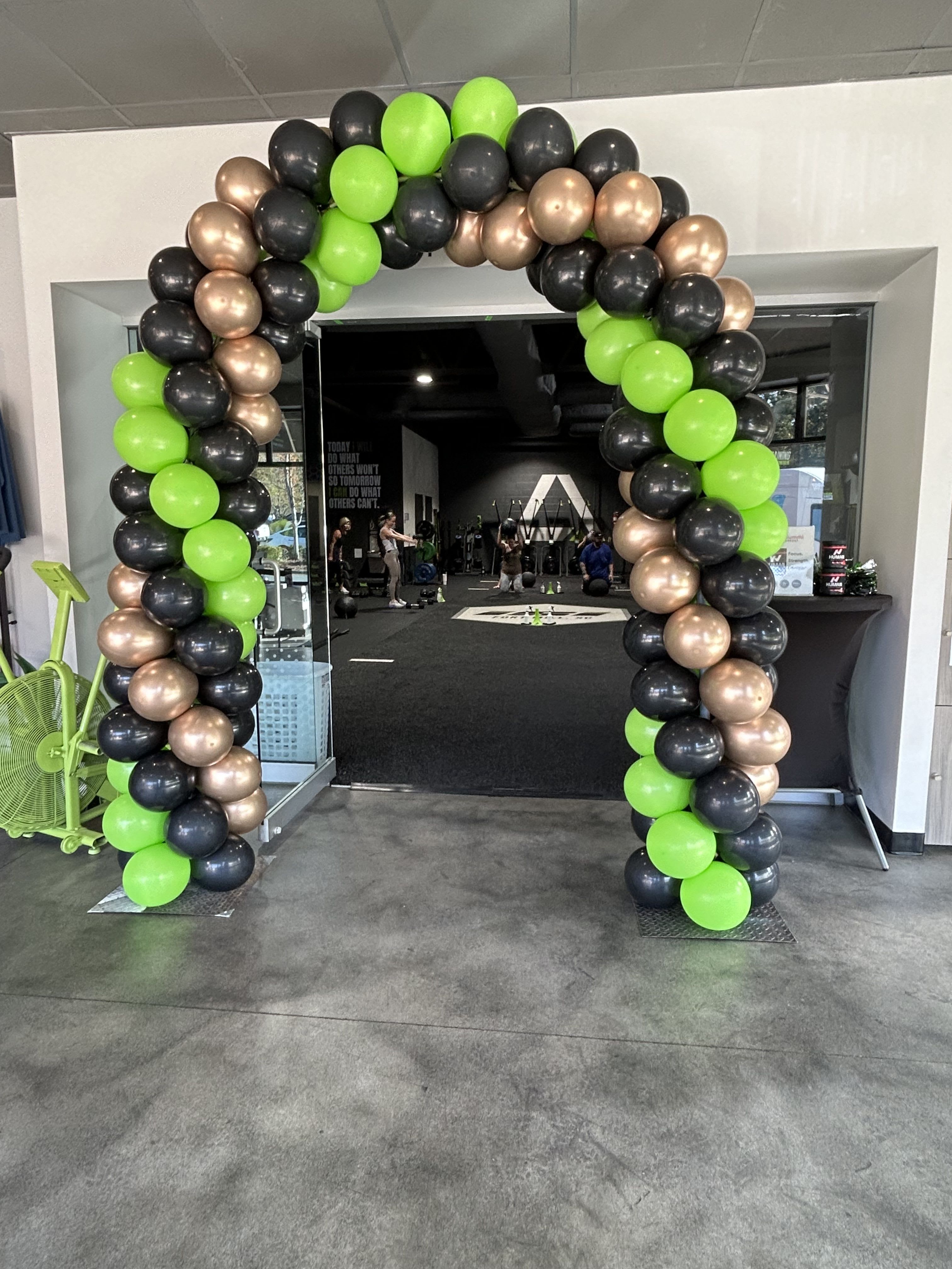 Balloon arch in neon green, black, and metallic gold at a gym entrance.