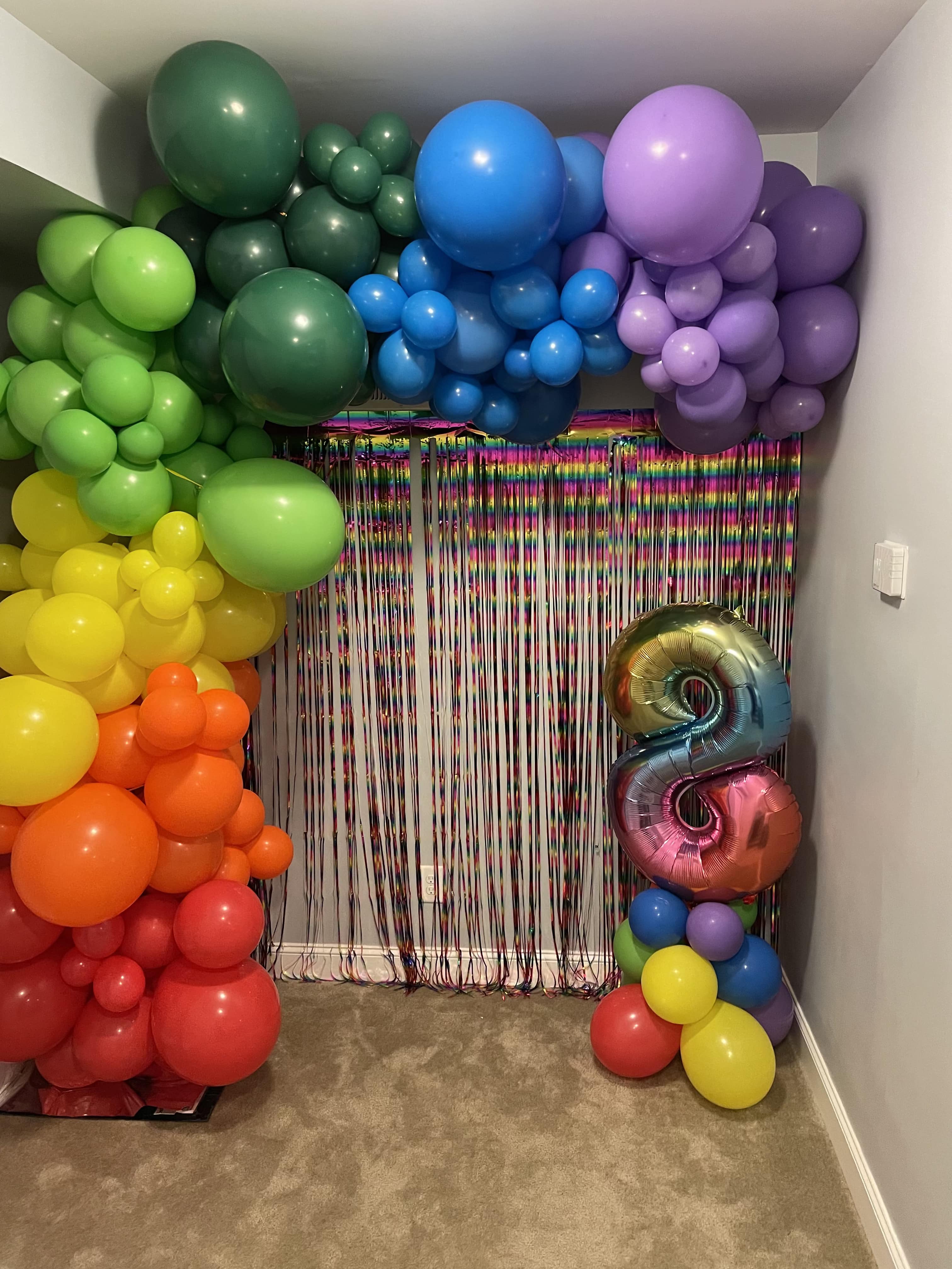 Rainbow balloon arch with a metallic number 8 balloon and fringe backdrop