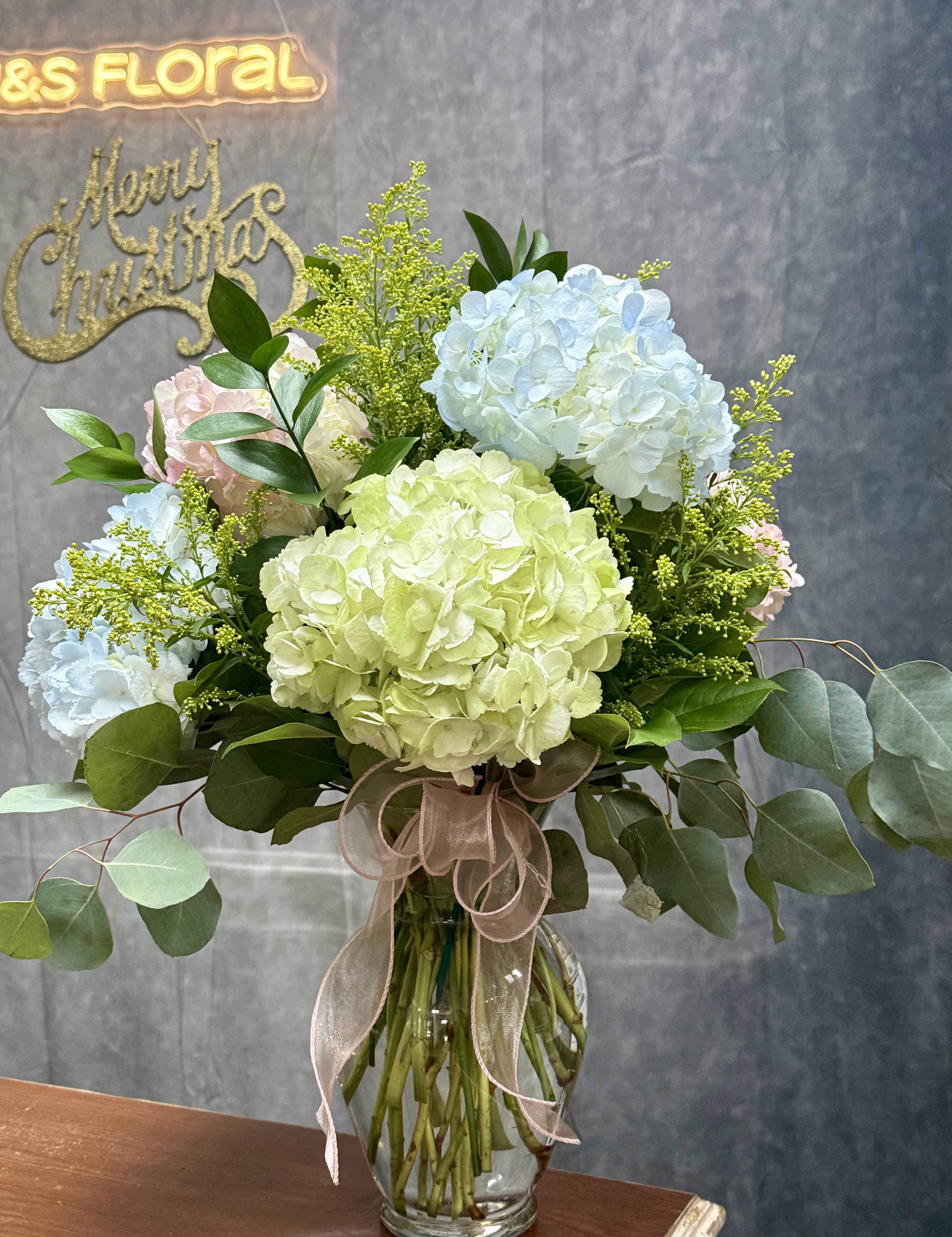 Hydrangeas Hues  - This enchanting vase features a delightful arrangement of soft-colored hydrangeas, showcasing a stunning blend of pastel hues. Each bloom exhibits delicate shades of pink, lavender, and cream, creating a soothing visual appeal. The voluminous petals and lush greenery add depth and texture, making this bouquet a perfect centerpiece or gift. Ideal for any occasion, this hydrangea arrangement brings a touch of elegance and serenity to any space.