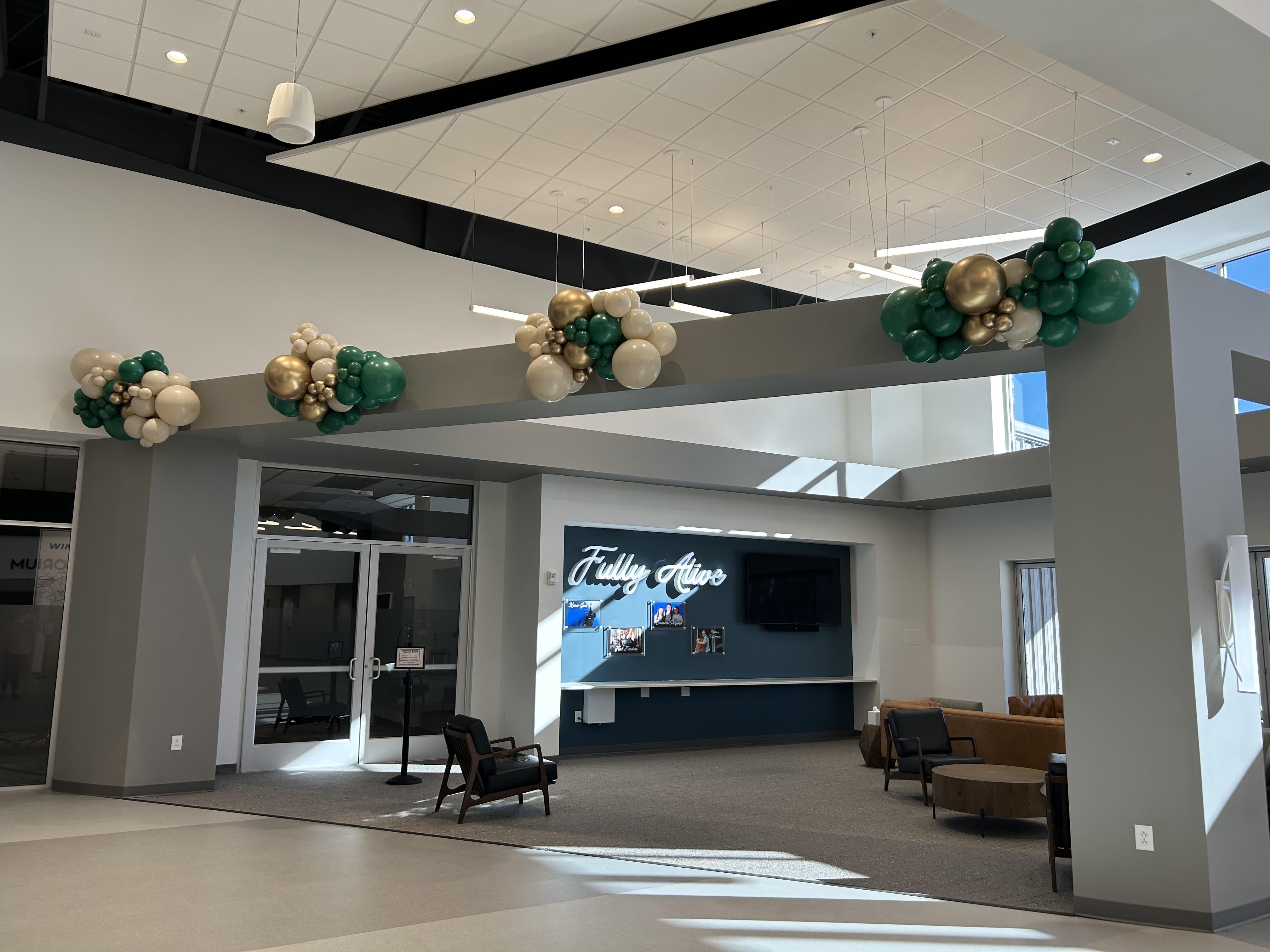 Balloon clusters in green, white, and gold hang from a lobby beam.