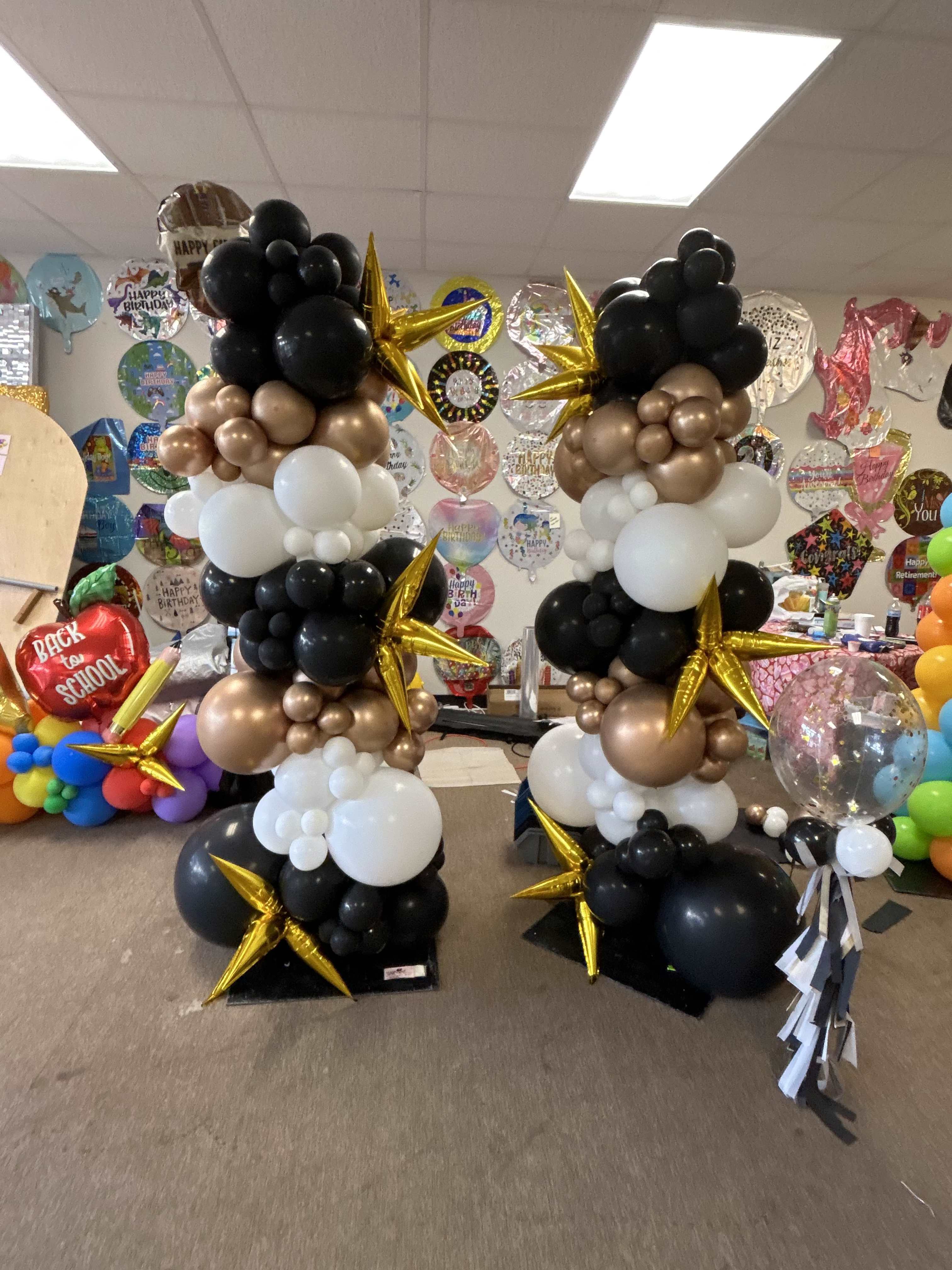 Two tall balloon columns in black, white, and gold with star balloons