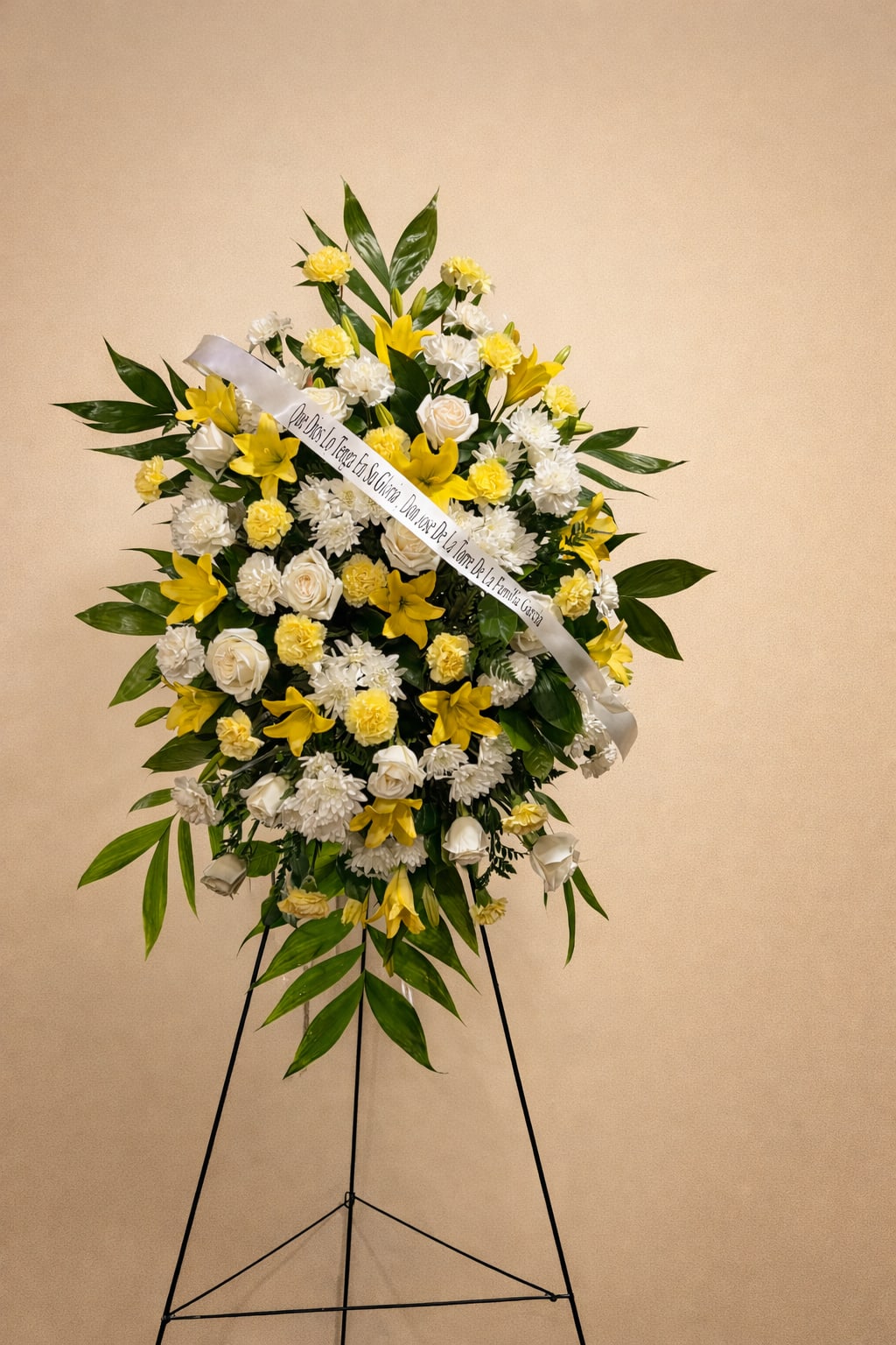 Golden Peace Premium Standing Spray - A radiant sympathy tribute featuring yellow lilies, white roses, and soft carnations, surrounded by a lush greenery this elegant standing spray, symbolize, peace, remembrance, and hope offering a beautiful way to honor and celebrate the life of a loved one displayed on a easel It creates a comforting presence at a funeral services or memorials. 