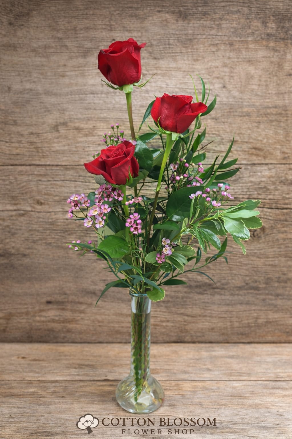 Three red roses in a clear glass vase with pink filler flowers