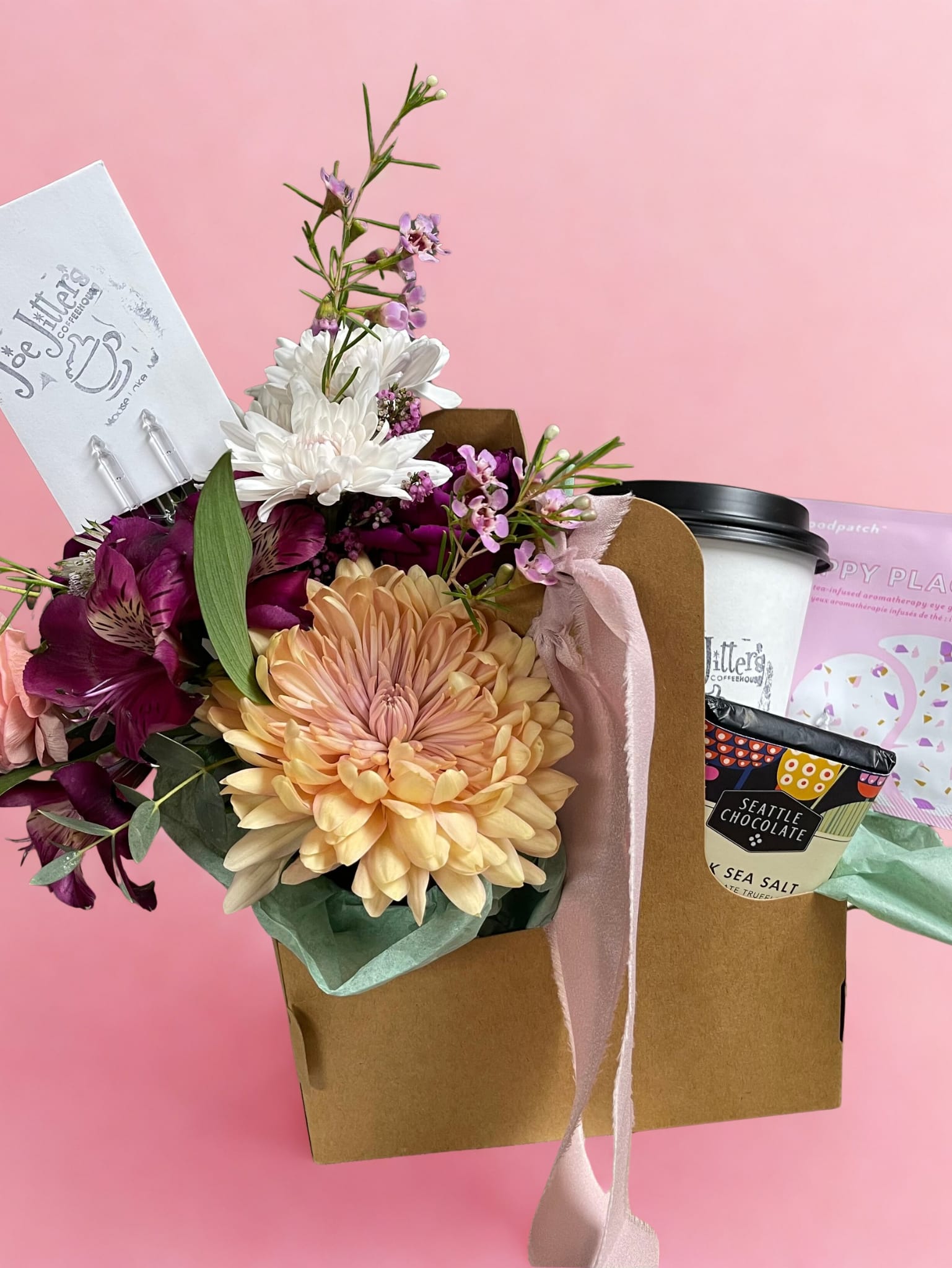 Petals &amp; Perks - Treat someone special (or yourself!) with our thoughtfully curated bundle that blends beauty, indulgence, and a touch of self-care. This charming gift includes:  Designers Choice Floral Arrangement: A stunning bouquet of fresh, seasonal blooms in romantic hues, carefully crafted by our expert florists.  Joe Jitters Coffee Shop Gift Card: Treat them to their favorite coffee or sweet indulgence from our beloved local coffee shop, Joe Jitters with a $10 gift card.  Gourmet Chocolate Bar: The ultimate sweet treat.  Eye Gel Patches: A little touch of luxury for a refreshing and radiant glow.   Beautifully wrapped in a coffee-themed tote with a satin ribbon. Perfect for birthdays, thank-yous, or just because moments. Wrapped and ready to brighten anyone's day. Order yours today!   All flowers, colors, containers, and flavors are created and hand-picked by our designers and are subject to change due to availability. 
