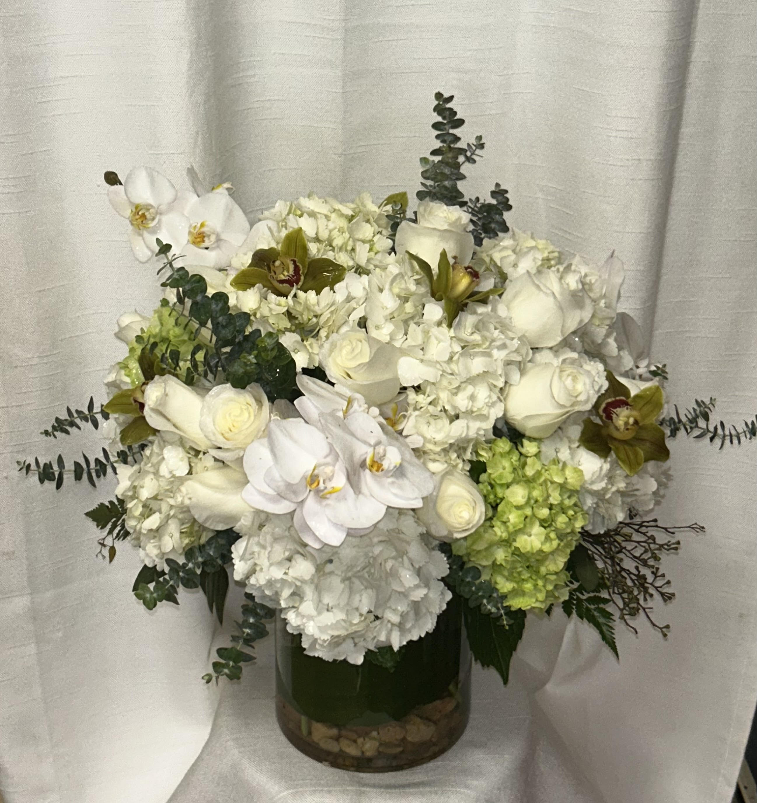 Lovestruck (DL) - Make a bold statement with our show-stopping modern floral arrangement, an elaborate and captivating display of natural beauty that is sure to impress. This mostly monochromatic arrangement features loads of fresh white hydrangeas arranged in a clear glass vase, creating a dramatic and striking centerpiece.   