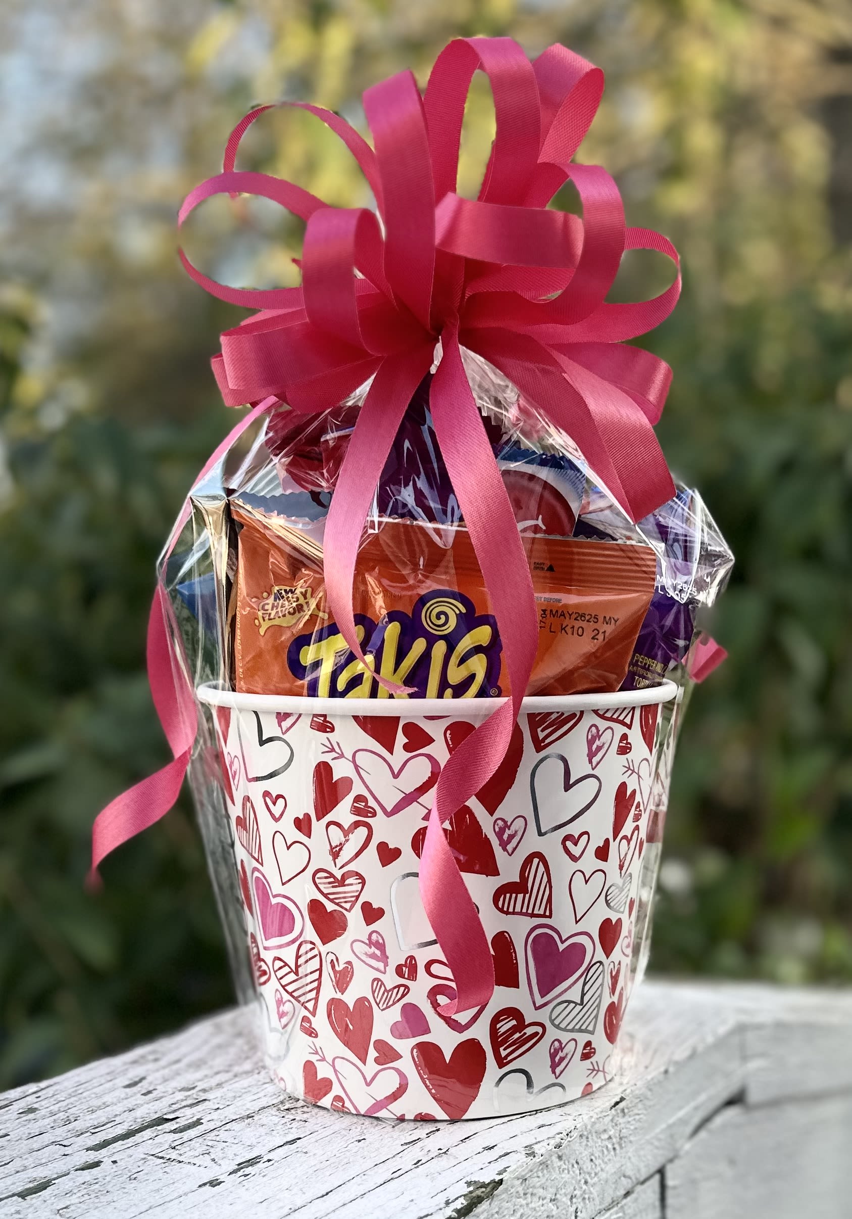 Snack Attack Bucket - Snack Attack Bucket  Indulge in the ultimate treat with our Snack Attack Bucket, a fun and festive collection of all your favorite snacks. Wrapped in clear cellophane and topped with a colorful bow, this bucket is filled with a delicious assortment of chips, cookies, crackers, candy, and more. Perfect for any occasion or as a special gift for someone who loves to snack, it's a surefire way to satisfy cravings and spread joy!             
