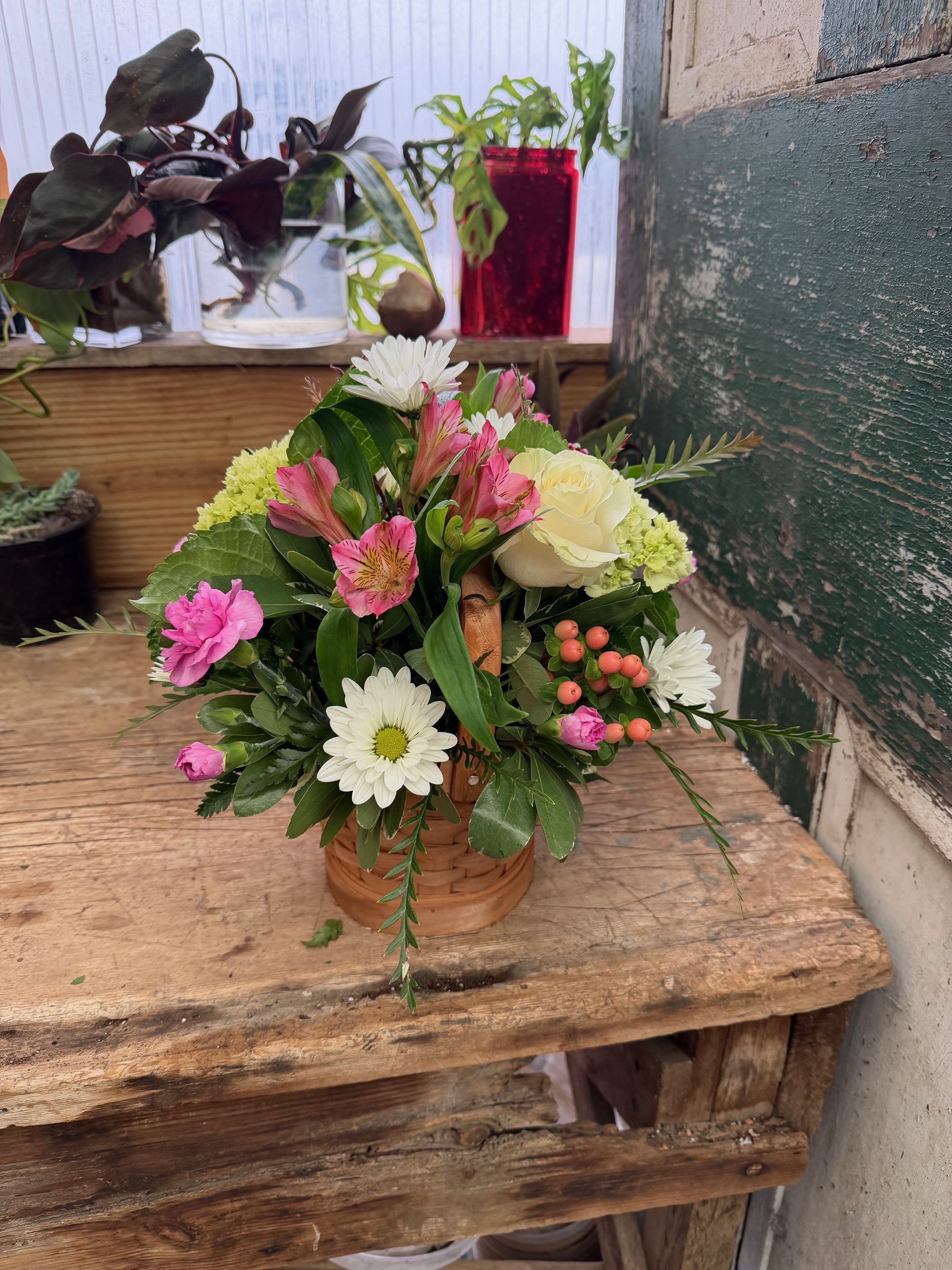 Mixed flower arrangement in a small wicker basket with pink, white, and cream blooms