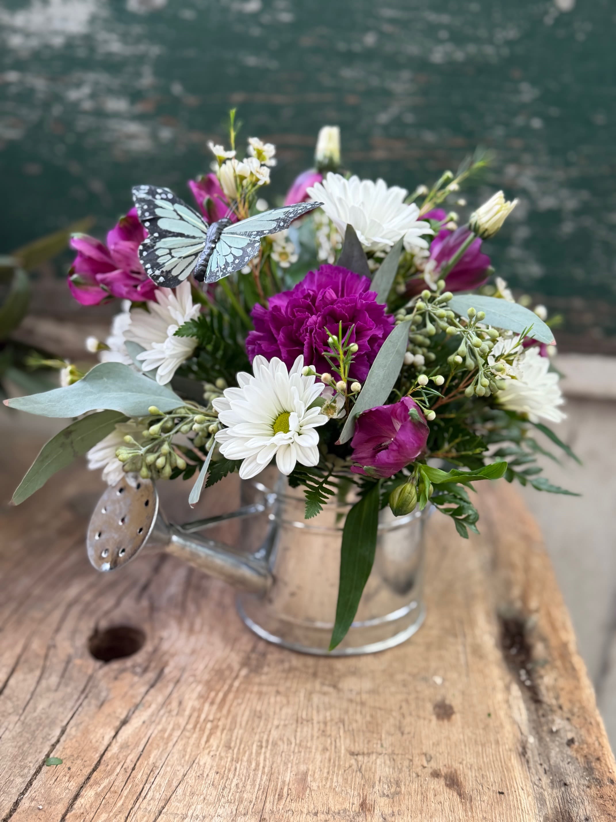 Bouquet of white daisies and magenta flowers in a clear glass mug with a butterfly decoration