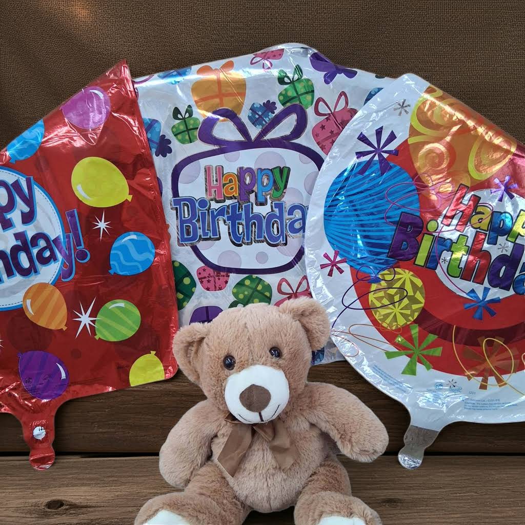 Teddy bear in front of three birthday balloons