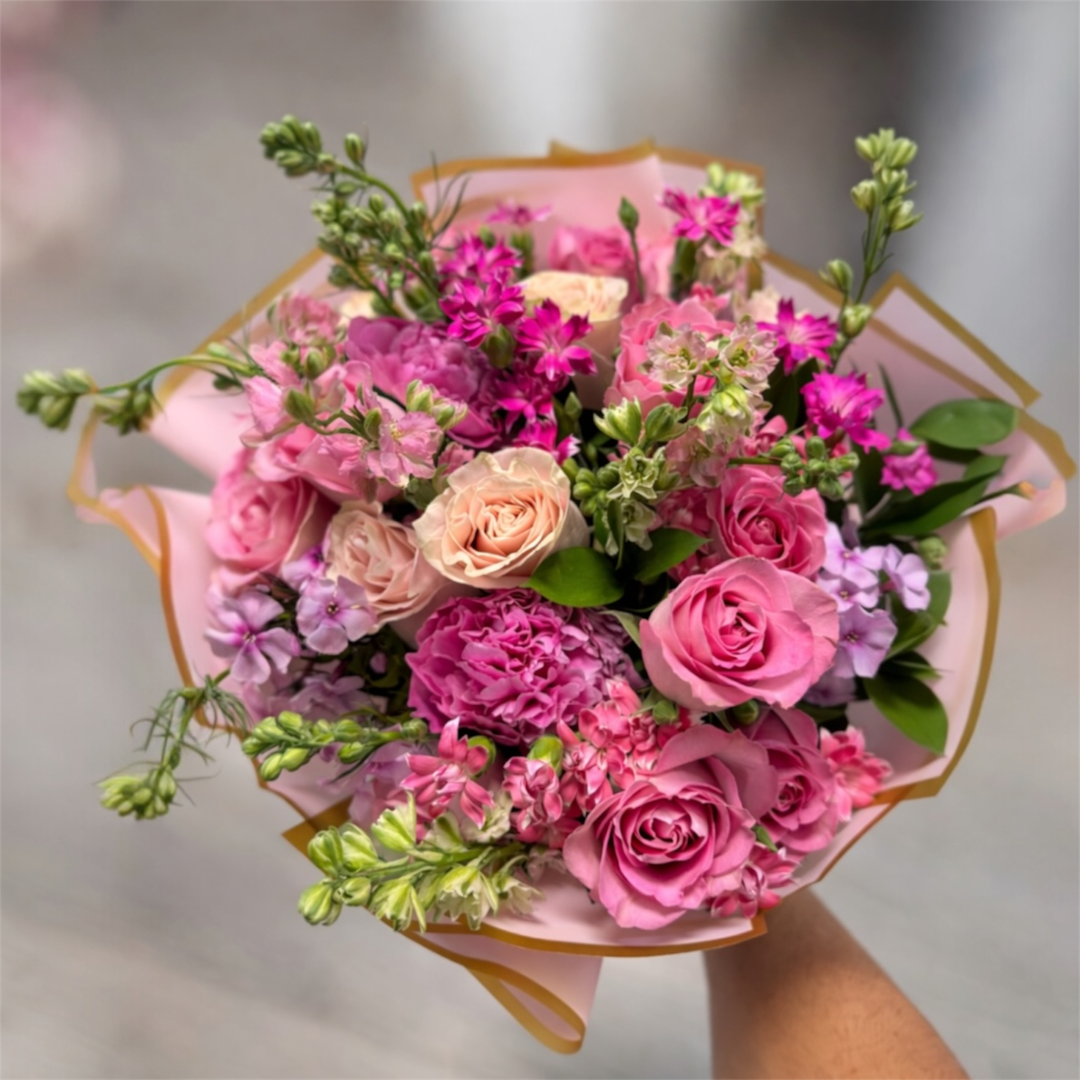 Pink Garden Charm - A romantic bouquet featuring soft pink roses, delicate seasonal blooms, and fresh greenery, beautifully wrapped in blush paper with gold trim. Elegant, feminine, and perfect for celebrating love, birthdays, or simply brightening someone’s day.