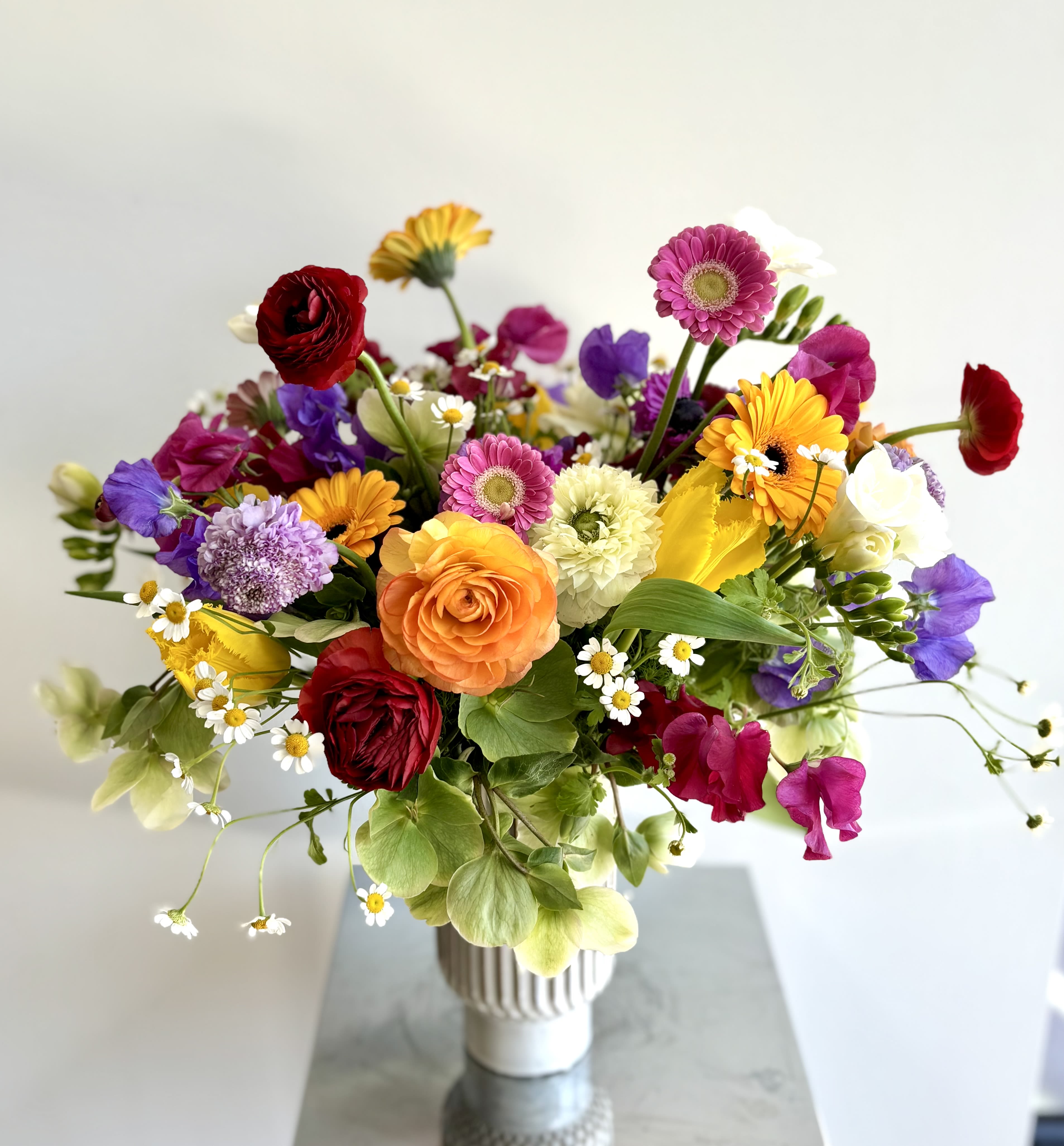 Blooms that Tell a Story - A gorgeous bouquet of abundant amount of premium spring flowers in a beautiful tall ceramic vase. This colorful flower gift offers a lovely selection of tulips, anemones, sweet peas, gerber daisies, hellebores, ranunculus, freesias, scabiosa, dianthus, and additional dainty blooms to fill the vase.