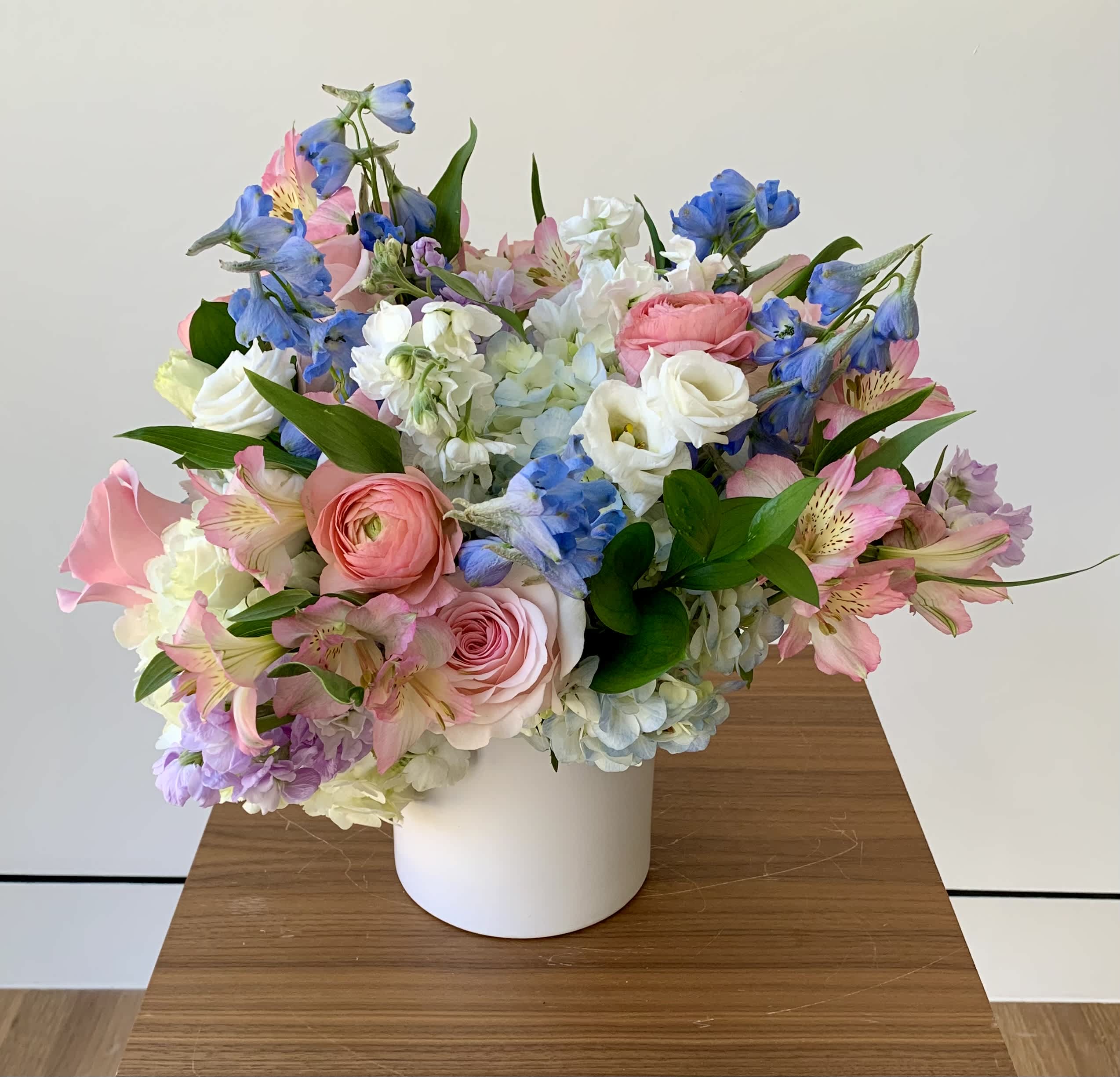 Lucky Girl - Colorful flower arrangement with premium flowers arranged in an white ceramic cylinder vase to bring joy and luck, with focus on peach, pink, blue and lavender colors. Michaela carefully selects premium and most fresh flowers to create a charming flower gift. Flowers may vary based on the availability. 