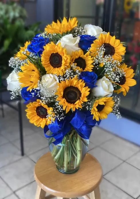 Sunshine Bouquet (Blue Edition) - Brighten up a table with a sprinkle of sunshine and brighten someone's day with this summer flower arrangement. Bold sunflowers and blue and white roses are arranged nicely in a clear vase.