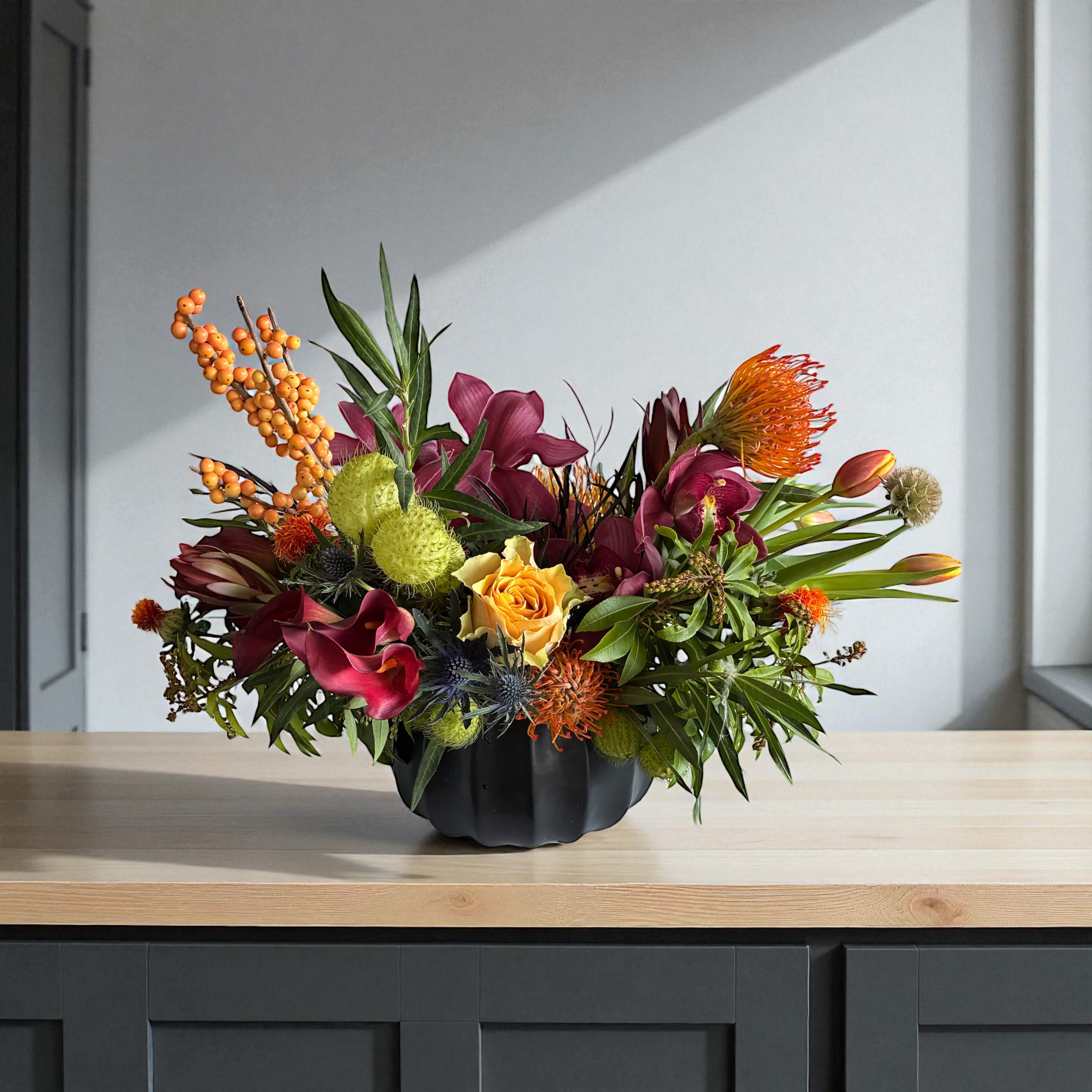 Colorful floral arrangement in a black vase with orange berries and burgundy blooms