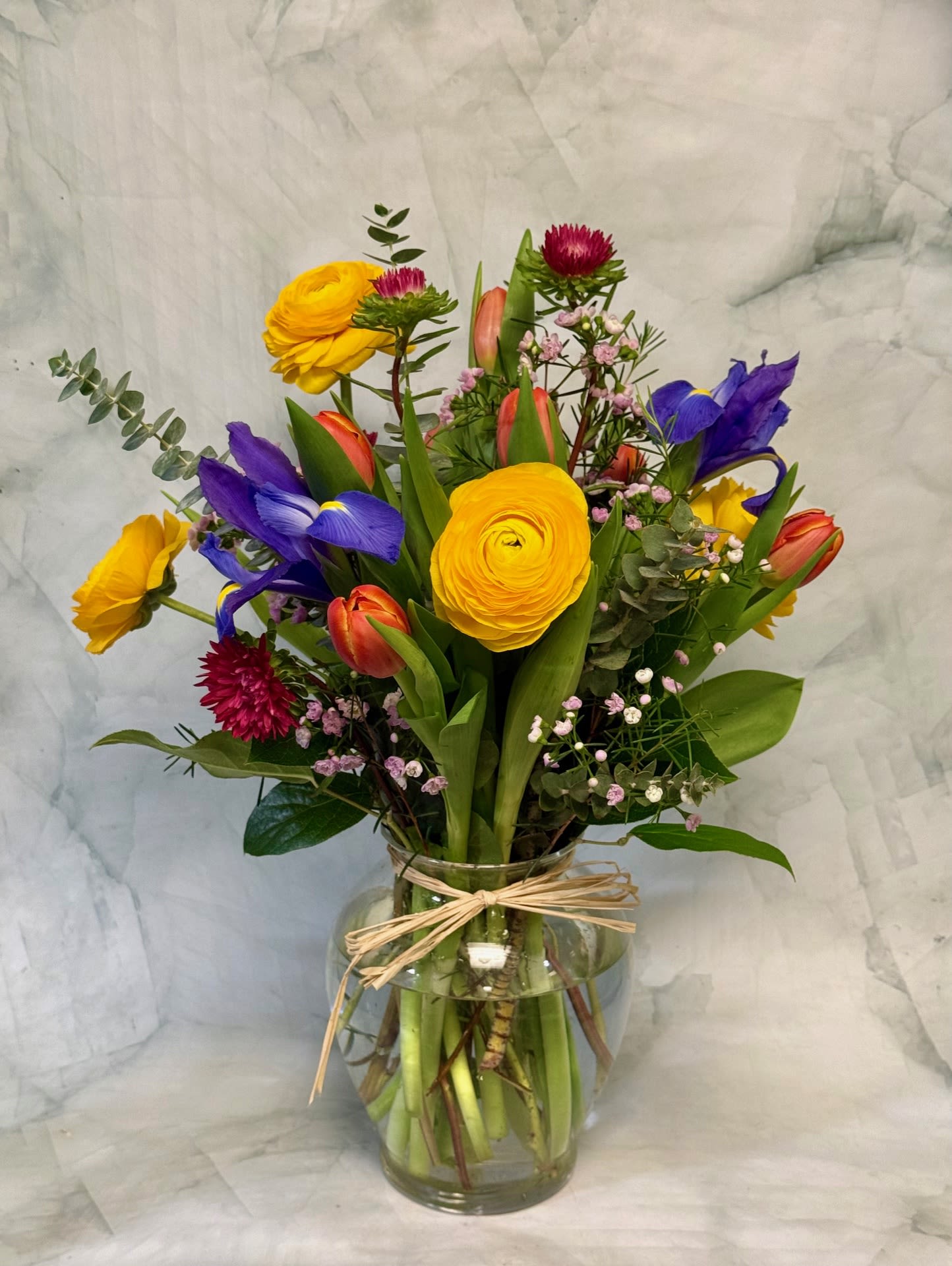 Springtime Celebration  - This colorful arrangement is a celebration of Spring. The flowers say Spring is here! There are Ranunculuc, Iris Tulips, Aster, Wax and Eucalyptus. 