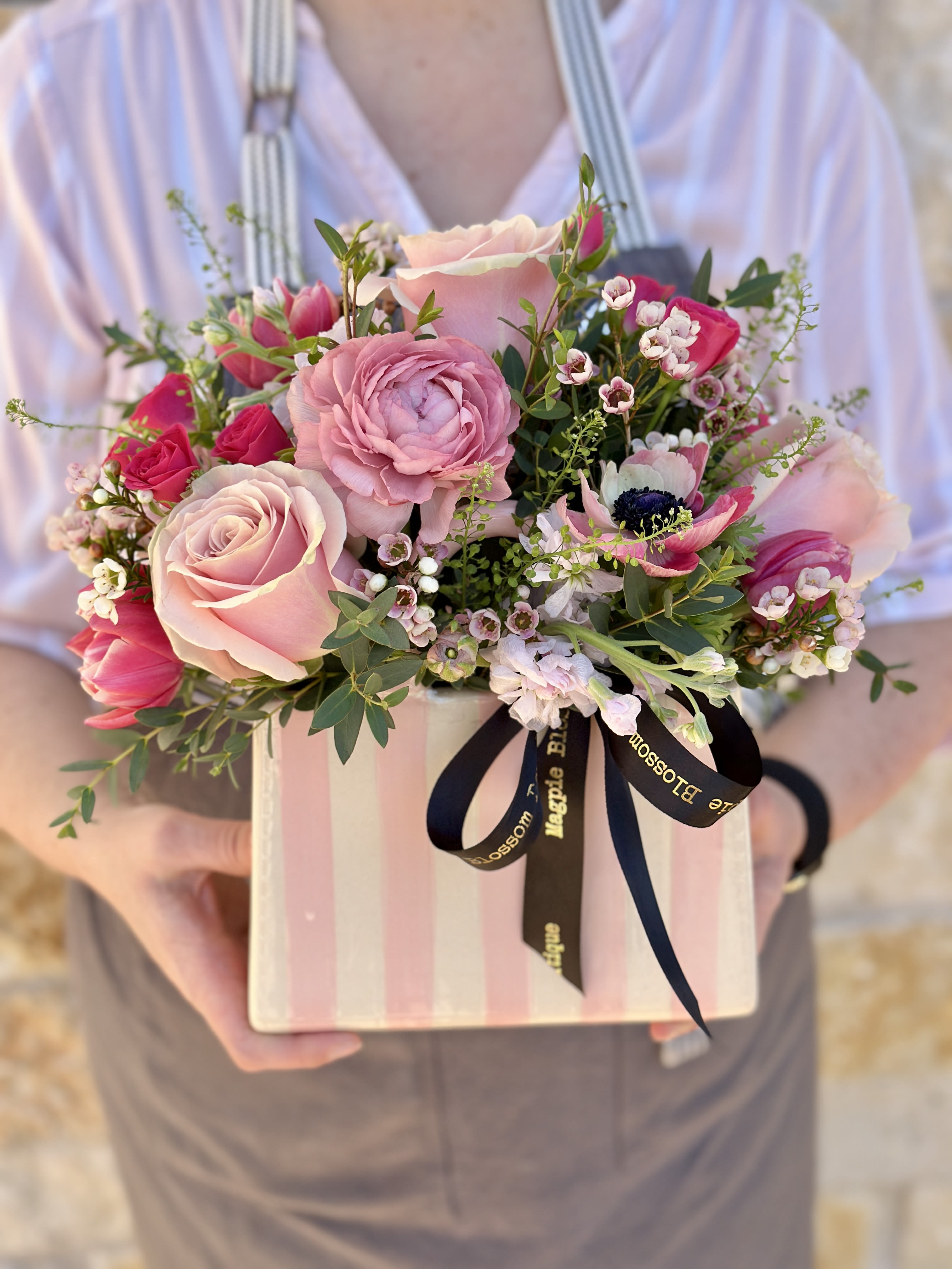 Miranda Pink Garden - Perfect for Mother's Day, Birthday, or a fun just because. Our ceramic Miranda Handbag Vase features white &amp; pink vertical stripes, a glossy finish, upright handles, and is versatile for repurposing as a fun display in the home once the flowers are done.  This adorable vase is filled with our prettiest seasonal pink blooms, foliage and accents.  Overall design is approximately 12" H x 14" W This is a one sided arrangement- meaning it's intended to be viewed from one side. Upgrade to deluxe to add more flowers &amp; make it two-sided. 