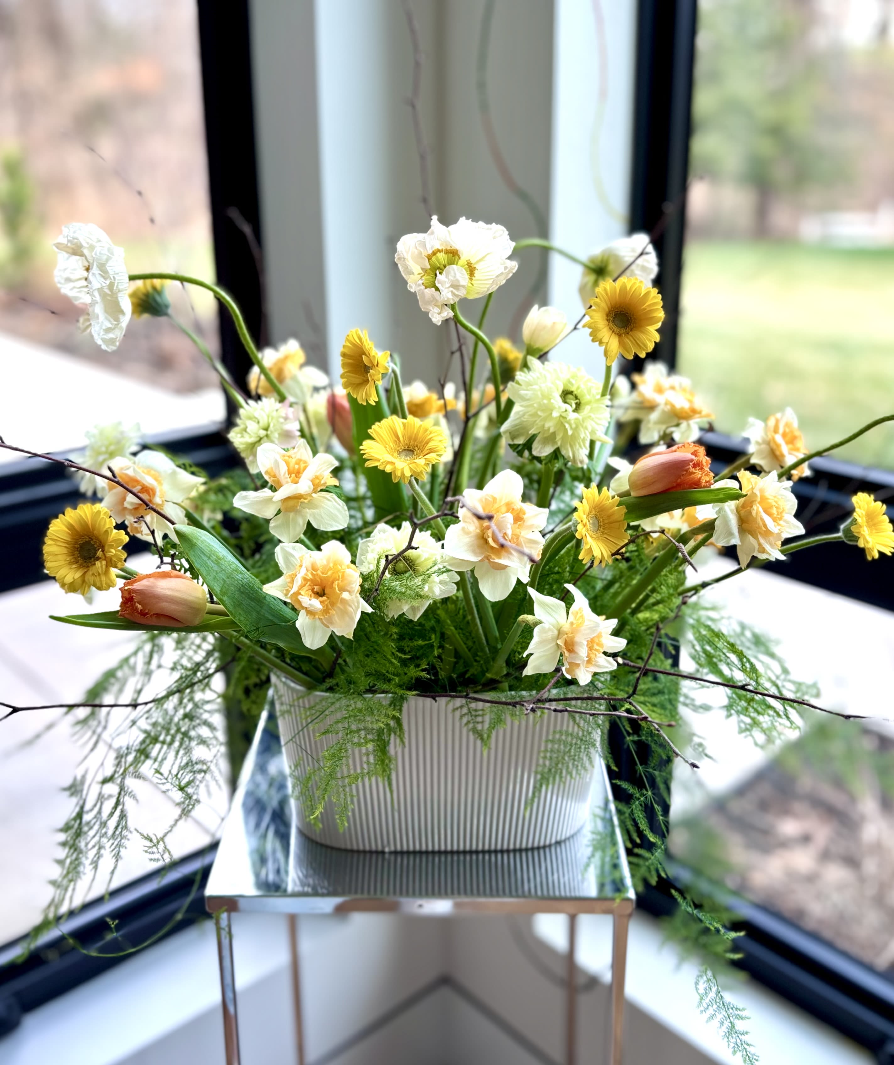 Easter Flower Centerpiece - Seasonal table centerpiece to celebrate Easter and Passover with premium spring flowers in the white and yellow color palette with a pop of orange and twigs arranged in a larger white ceramic oval vase. The mix of flowers is selected based on the availability of the most fresh flowers, usually tulips, ranunculus, poppies, daffodils, anemones, mini gerbers and greenery. 