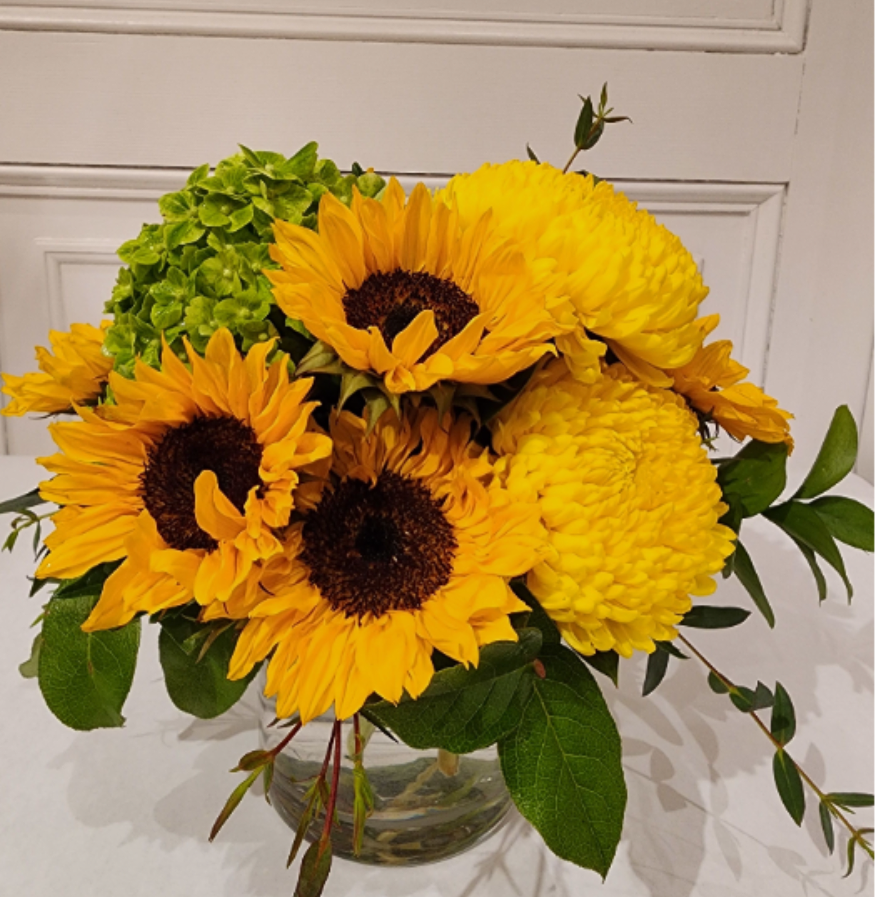 "Van Gogh" Bouquet - This sunny bouquet is inspired by the many paintings of the French Impressionist painter, Vincent Van Gogh. Bright sunflowers are the star of the show, accompanied by golden Cremones and green hydrangea. This is the perfect bouquet to lift a friend's spirits or spread a little sunshine just because.   