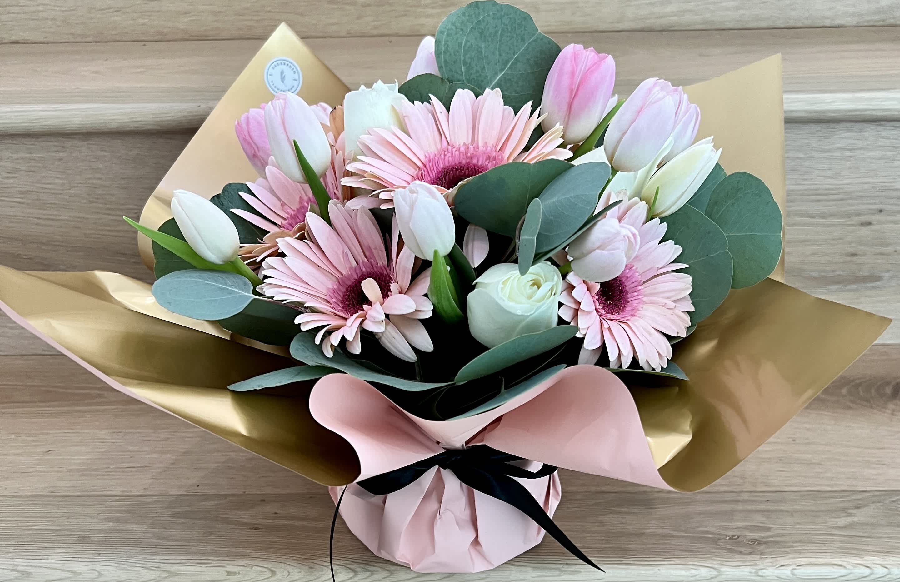 Bouquet of pink gerbera daisies and white tulips wrapped in gold and pink paper