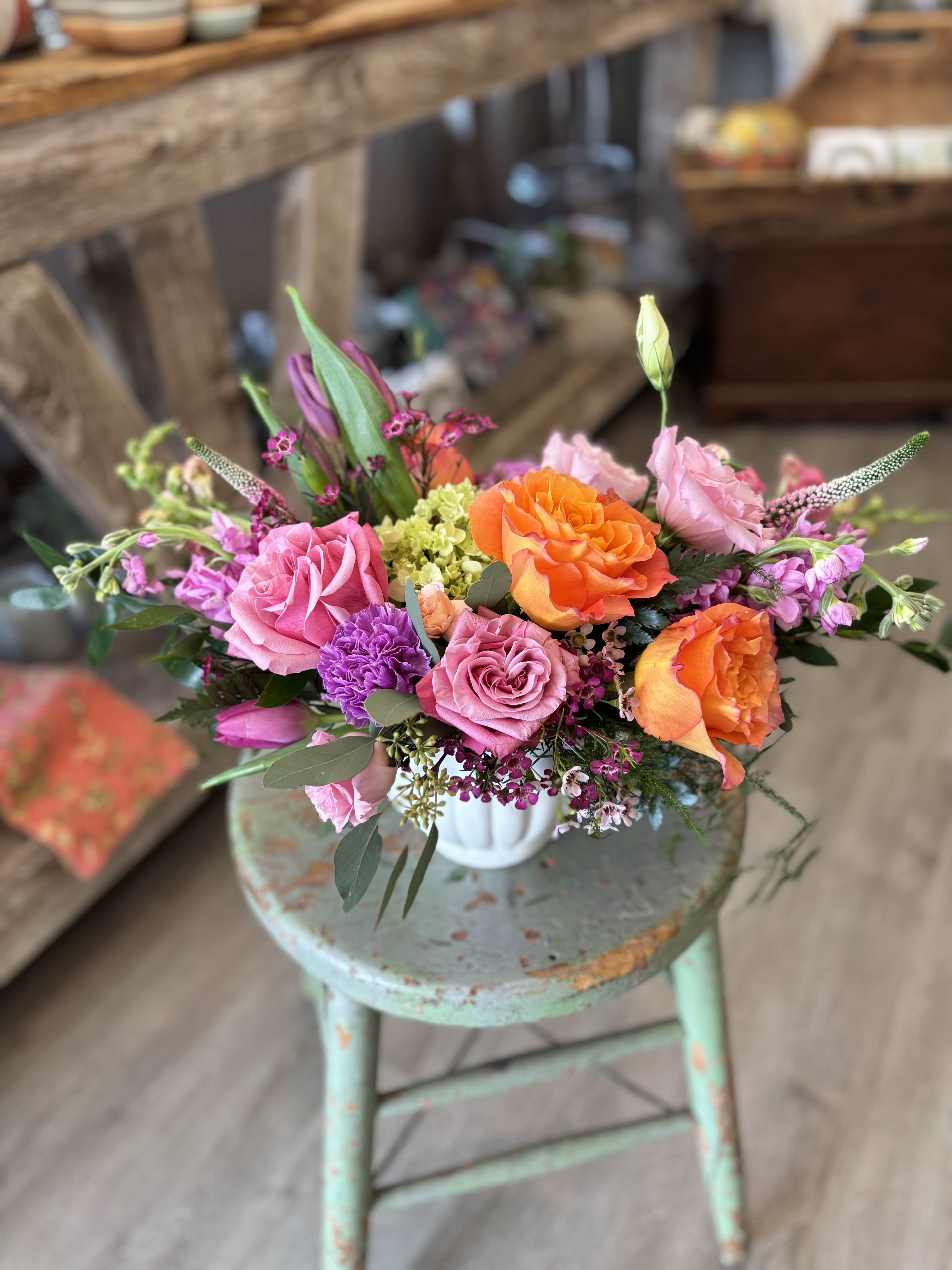 Jubilant Garden  - This joyful garden-style arrangement is filled with vibrant coral roses, fragrant lilac* and soft pink accent flowers. Designed in a charming fluted white vessel it has a fresh gathered from the garden feel. Perfect for Mother's Day or everyday, it's a bright and uplifting way to celebrate someone special.   *lilac is in season in May. Until then, lilac will be substituted with another lovely bloom. 