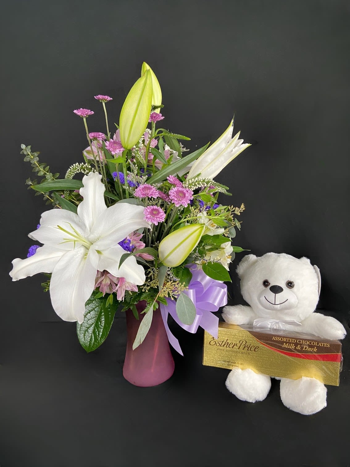 Rosy Bear! - Why give 1 gift when you can give three? This big bundle is packed with a 1/2lb box of assorted Esther Price chocolates, medium stuffed teddy bear, vase arrangement of fresh cut white oriental lilies with lavender and white accent flowers.
