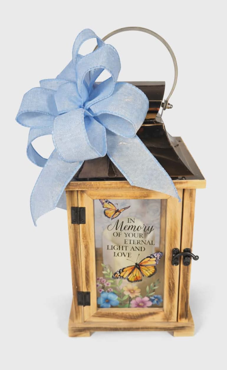 Memory of Your Eternal Light Lighted Lantern -  "In Memory of Your Eternal Light and Love". This lantern is made from quality wood and a stainless steel copper finish top. It features a built-in automatic timer which runs for 6 hours on and 18 hours off(3-AAA batteries are included) and is uv printed with a sentimental quote. Suitable for hanging or free-standing use inside. Comes adorned with a beautiful matching bow.  Choose Deluxe if you would like to add a Silk Arrangement on the lid of the lantern.   W: 6 1/4" H: 13 1/2 " D: 6 1/4 "