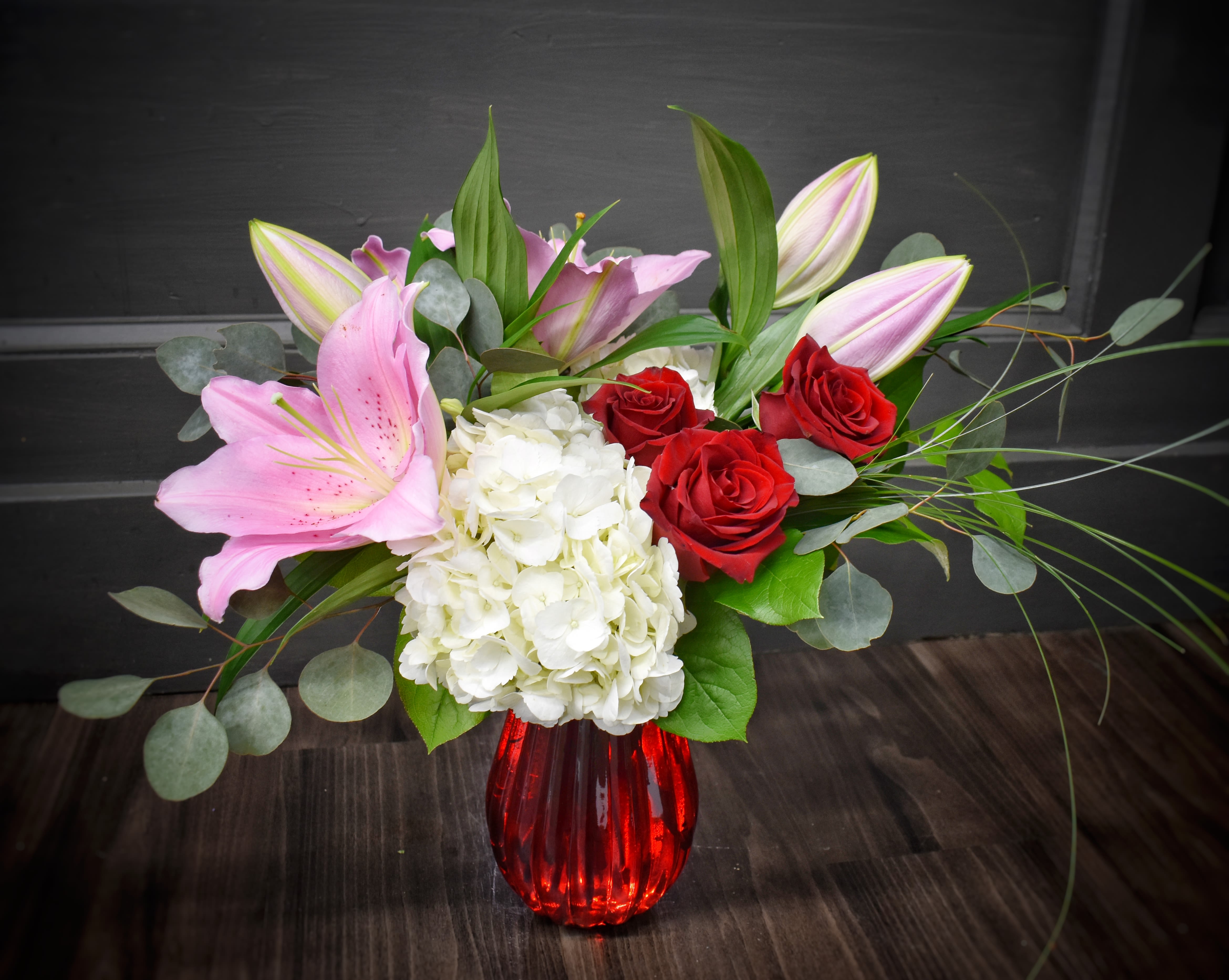 Ruby Radiance - We've designed this bouquet in a ruby red vase with fluffy white hydrangeas, fragrant pink lilies and red roses accented with a variety of foliages. In the deluxe and premium versions we'll add more roses!
