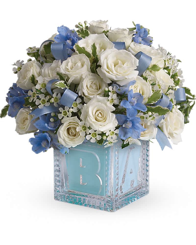Baby's First Block by Teleflora - Blue - Celebrate the coolest baby boy on the block's arrival with this charming glass vase that arrives chock full of pretty flowers. Perfect for baby showers, too! The glass block will make an adorable display piece for years! Dazzling white spray roses, light blue delphinium, white waxflower and light blue organza ribbon are delivered in a clear block with a light blue liner. One great delivery deserves another, don't you think?
