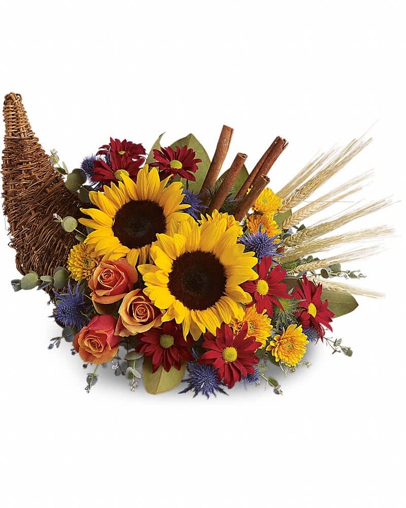 Classic Cornucopia - Along with joy, this cornucopia carries an abundance of beautiful fall flowers and foliage. A stunning centerpiece or inviting entryway display, this beauty will be at home anywhere in the house. Dazzling sunflowers, light orange roses and spray roses, red daisy spray chrysanthemums, yellow cushion spray chrysanthemums, eucalyptus, magnolia leaves, cinnamon sticks and wheat are perfectly arranged in a wicker cornucopia. Now you know why cornucopia translates to "horn of plenty."
