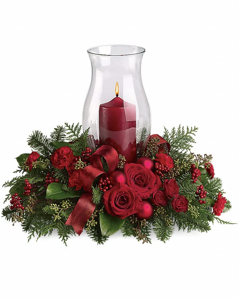 Holiday Glow Centerpiece - Glow ahead and send this spectacular centerpiece to anyone who's on your Christmas list this year. A glowing hurricane candle takes center stage but the surrounding festive touches make this arrangement radiate joy. Beautiful red roses, spray roses and carnations, white asiatic lilies, festive Christmas greenery and ornaments plus an elegant hurricane candle make this divine Christmas dÃ©cor.