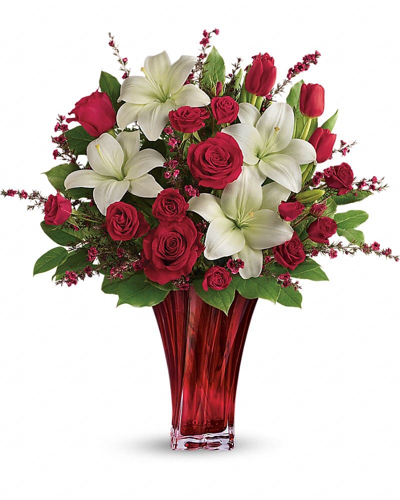 Love's Passion Bouquet by Teleflora - Classic romance is this radiant bouquet of red roses, crimson tulips and pure white lilies, hand-delivered on Valentine's Day or any day in an exquisite blown glass vase. With its radiant red hue and unique twisting shape, it's sure to take their breath away! This passionate display of red roses, red spray roses, red tulips, and white asiatic lilies is accented with red leptospermum, leatherleaf fern, and lemon leaf. Delivered in a Love's Passion vase.